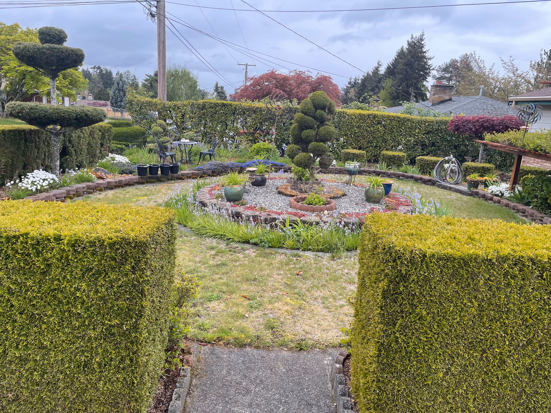 A manicured garden with trimmed hedges, topiary, potted plants, and a gravel central area.