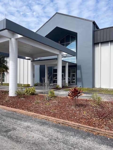 Modern building entrance with a covered drop-off and landscaped front area.