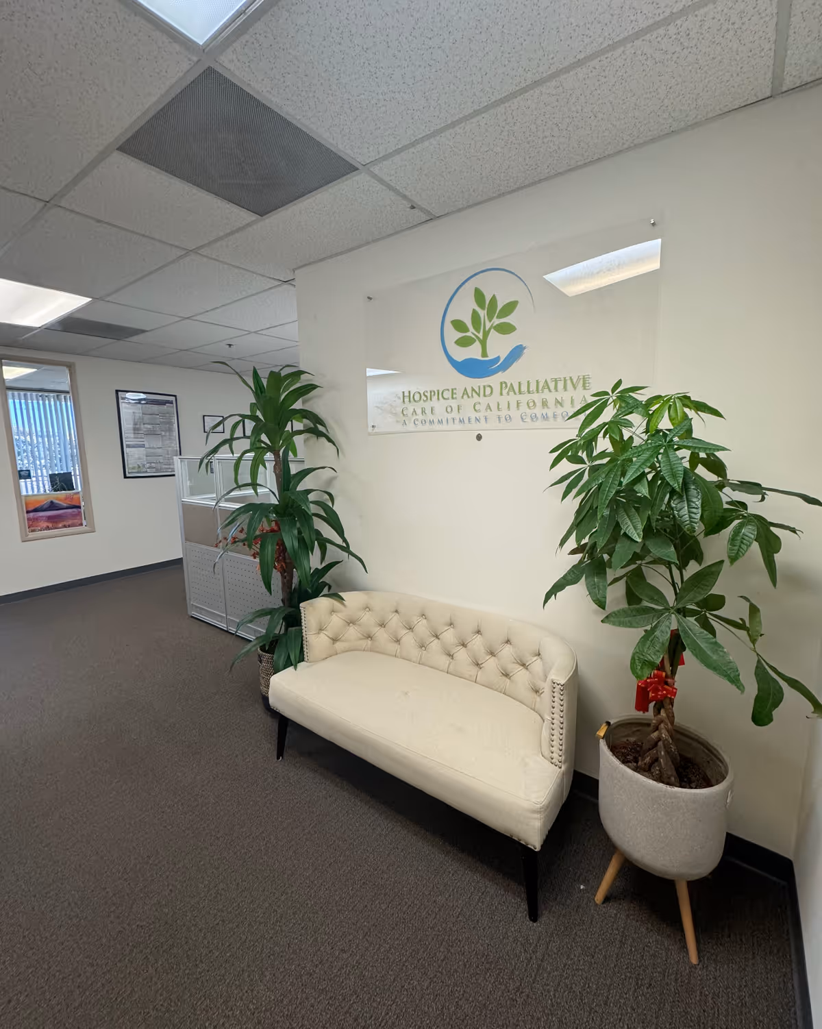 Lobby area with a beige sofa, potted plants, and Hospice and Palliative Care of California sign.