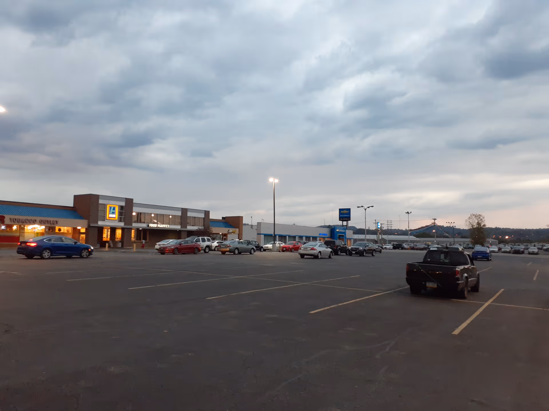 Wide parking lot in front of a blue-and-tan shopping center exterior under cloudy sky