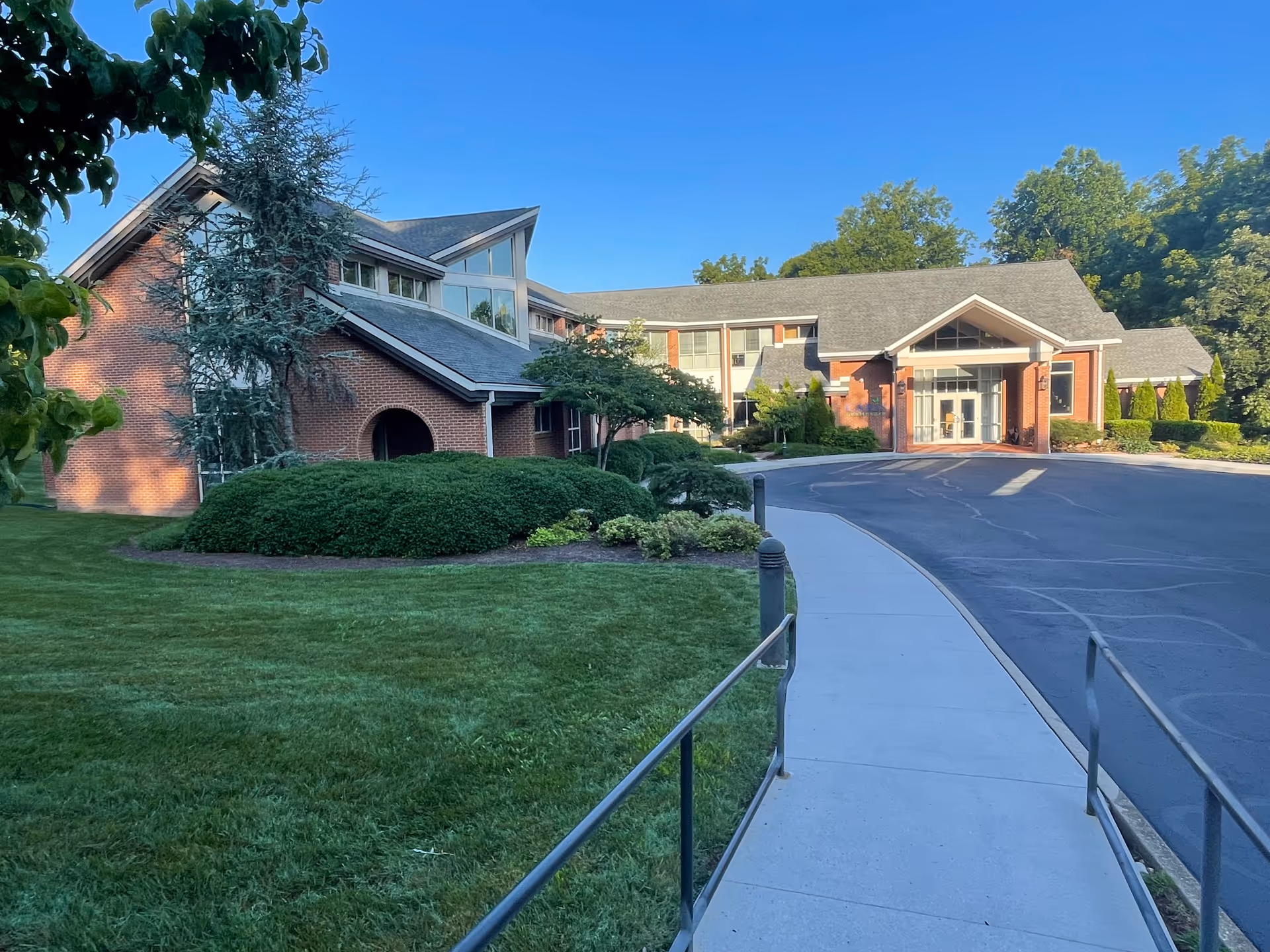Brick senior living facility with glass front entrance, curved driveway, and manicured landscaping.