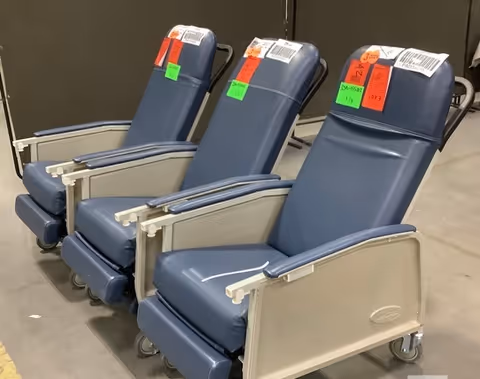 Three blue padded chairs on wheels with price tags in a storage area.