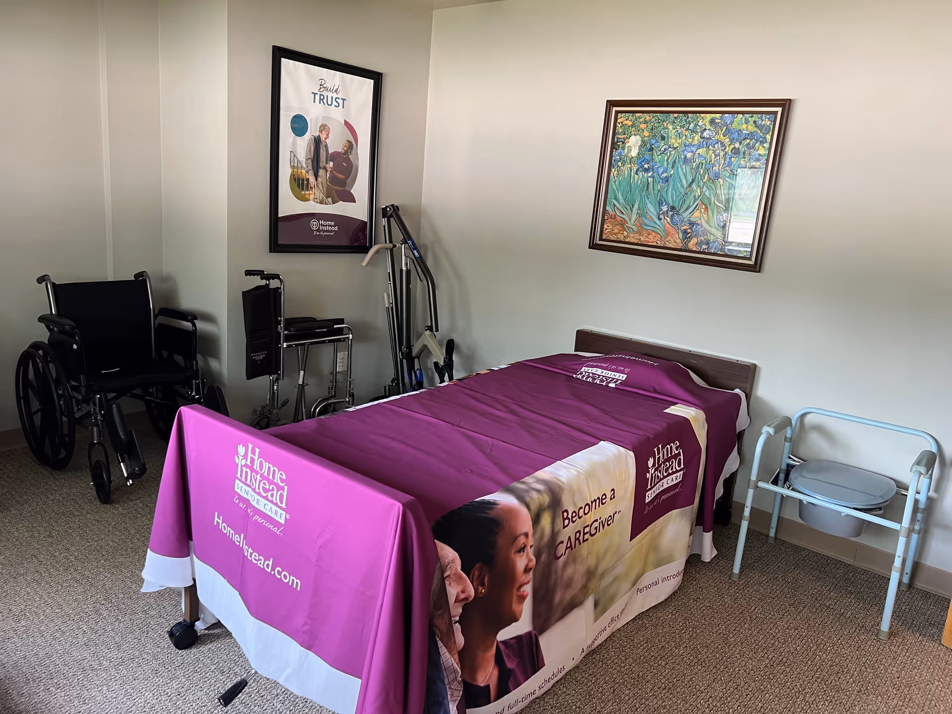 A small care room with a purple Home Instead bed cover, wheelchair, walker, and equipment.