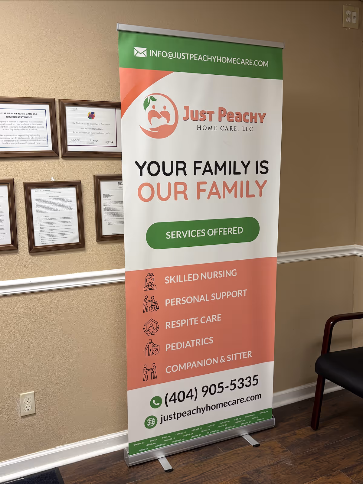 Banner for Just Peachy Home Care stands in a hallway beside framed certificates