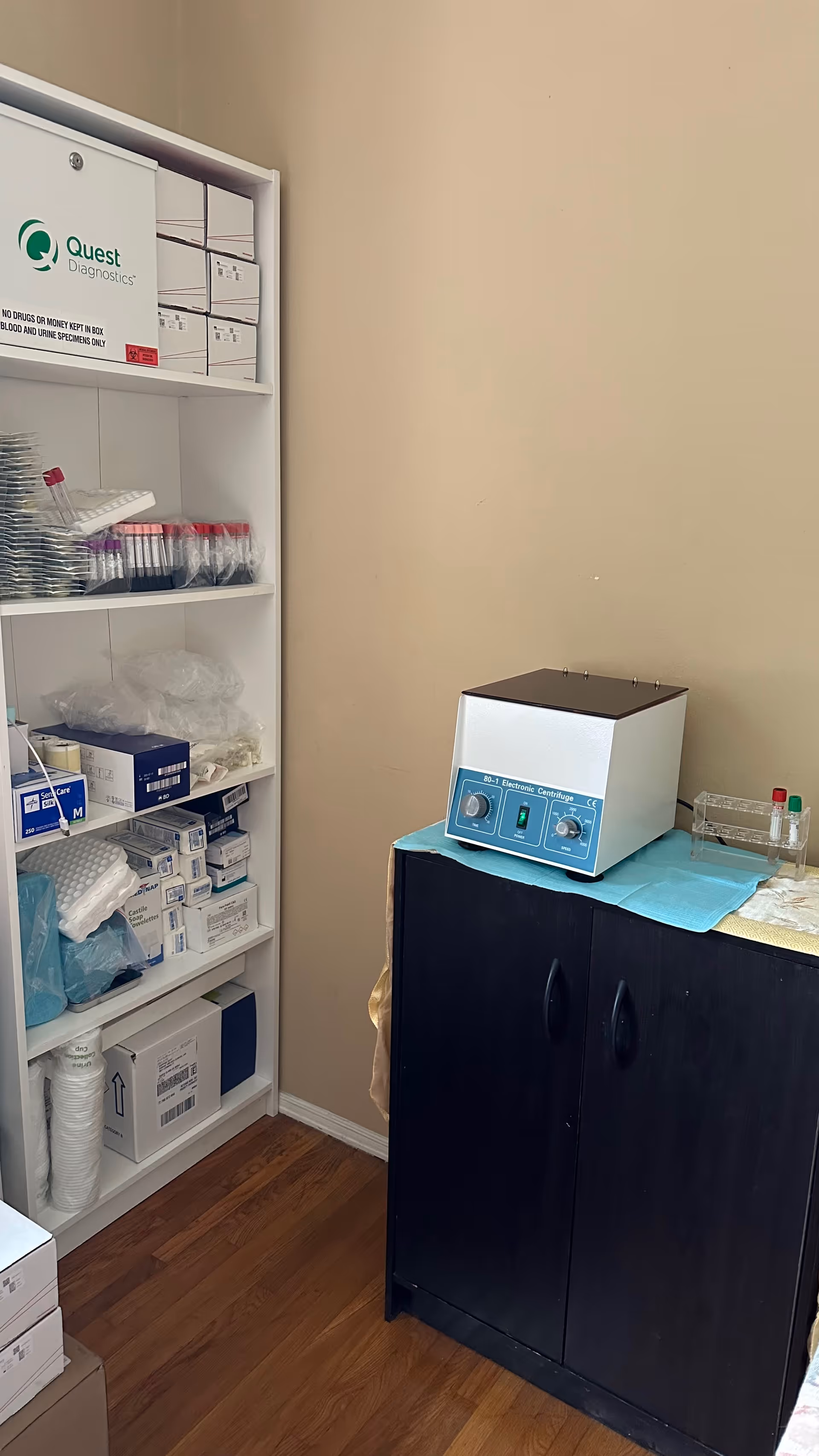 Medical supply shelves and a benchtop lab device in a small clinic room.
