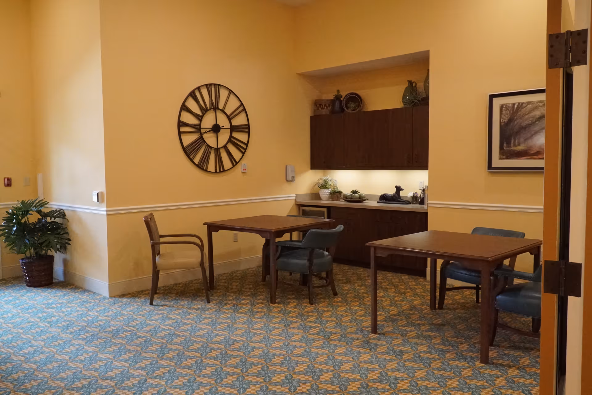 Common area with tables, chairs, a kitchenette, wall clock, and framed art.