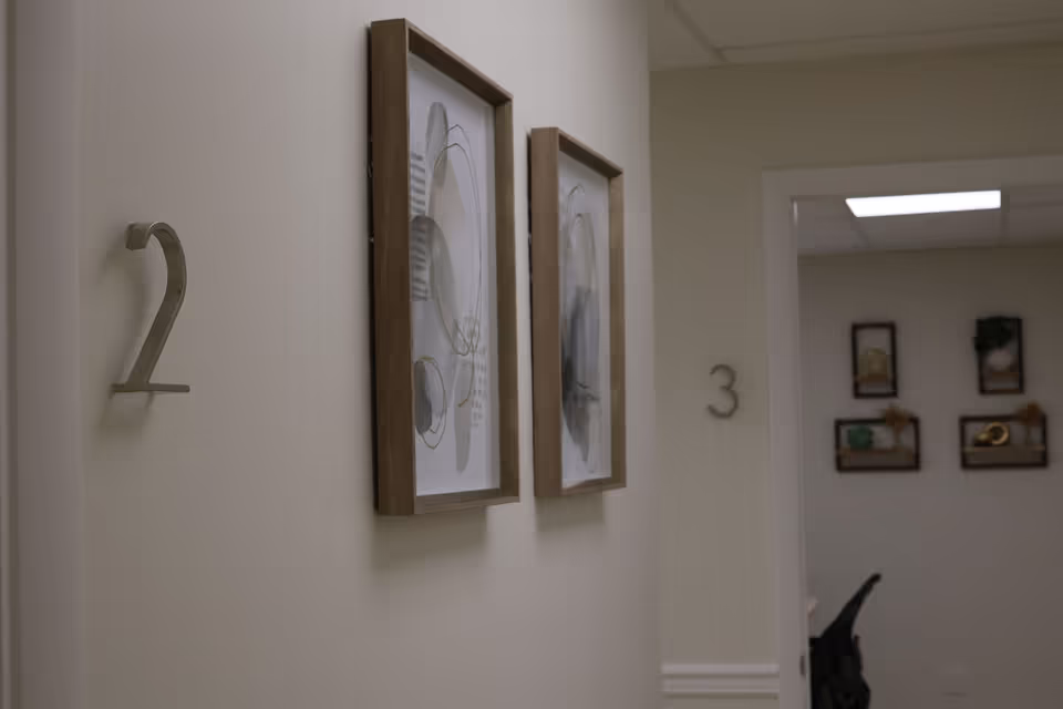 A corridor in a senior living facility with numbered doors and framed art.
