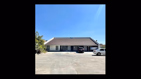 Single-story facility with a covered front entrance and two parked cars in a sunny lot.