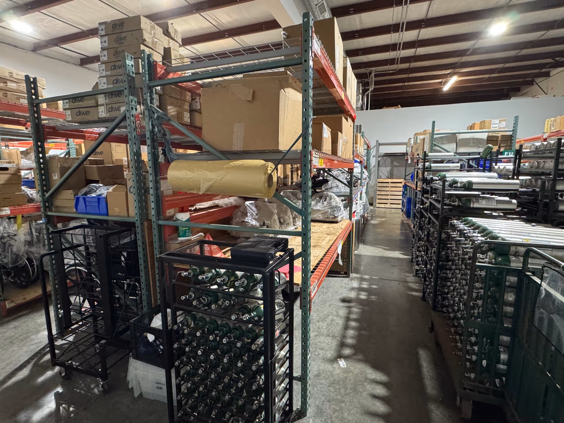 Industrial storage room with tall metal shelves, boxes, rolls, and stacked supplies.