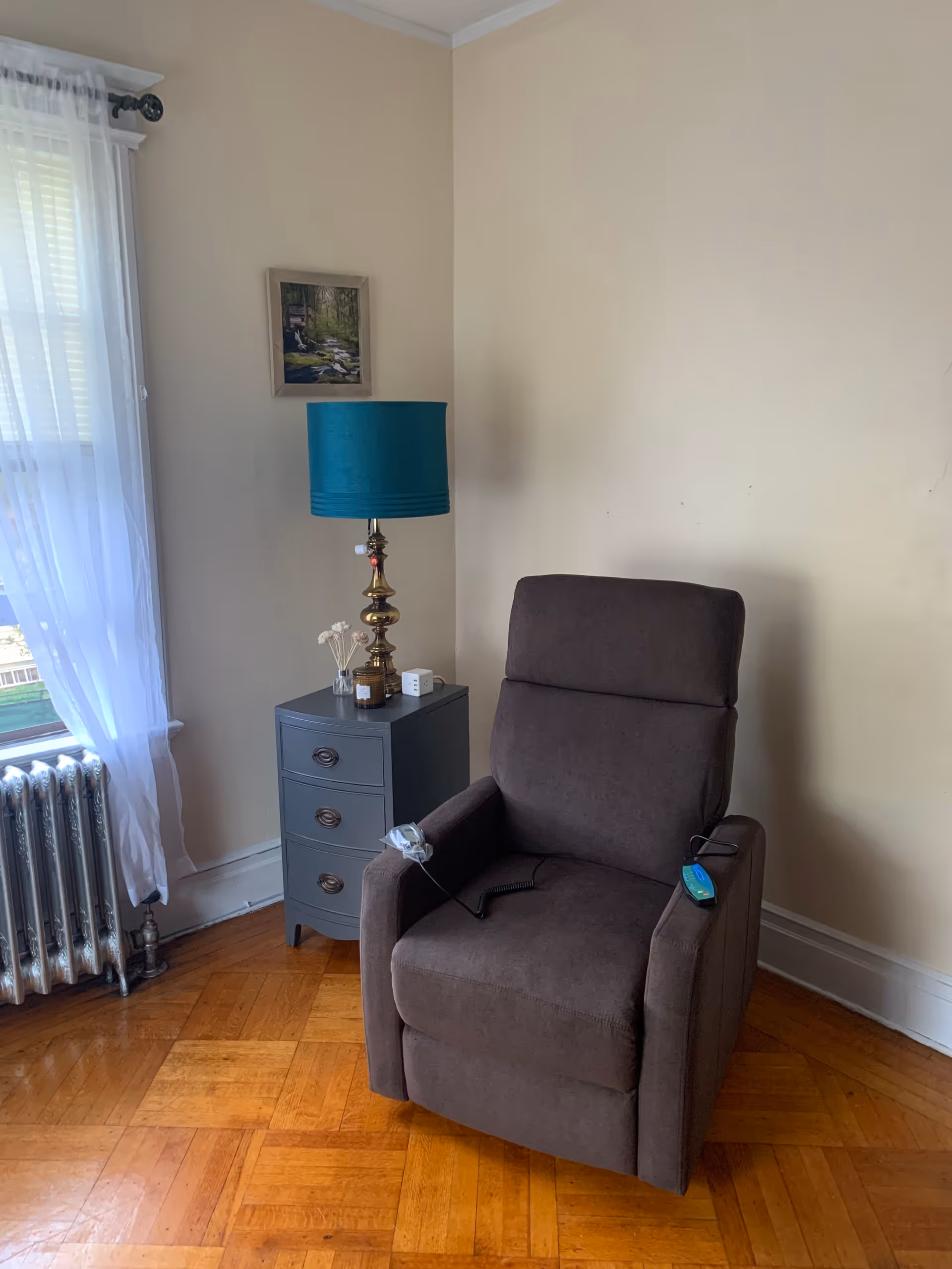 A brown recliner chair beside a gray side table with lamp in a sunlit living room.