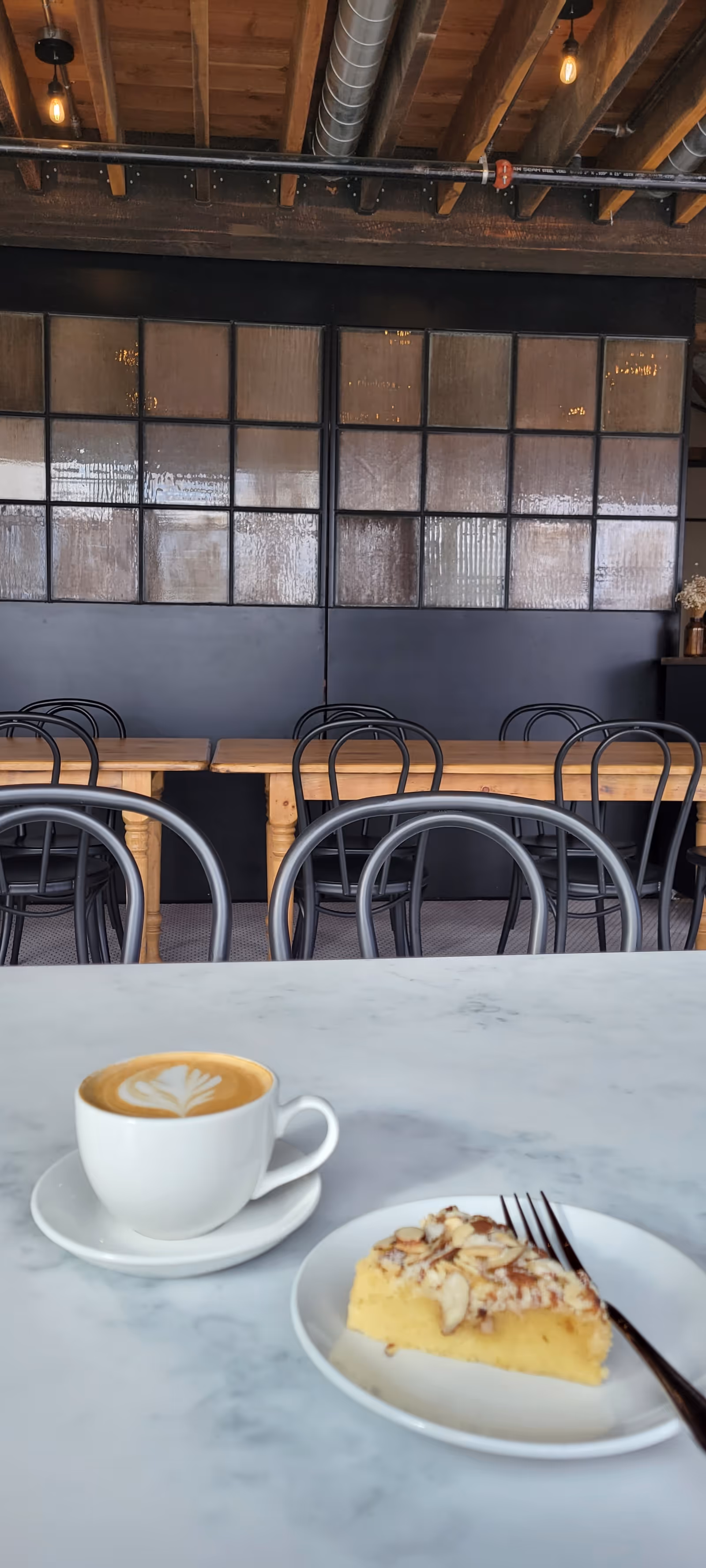 Cafe-style dining area with marble table, latte, cake, and empty chairs.