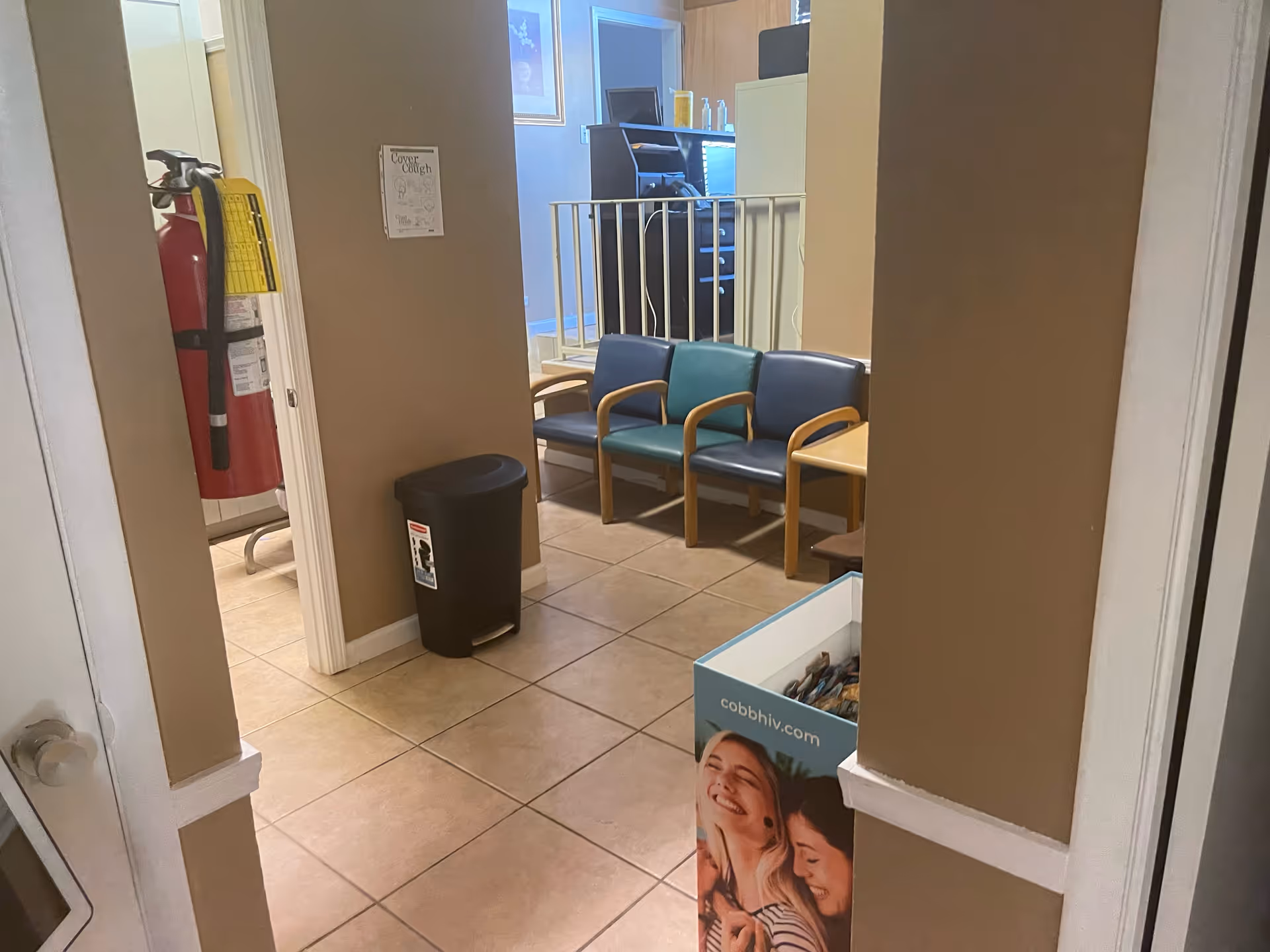 Lobby waiting area with beige walls, tiled floor, chairs, and a brochure box.