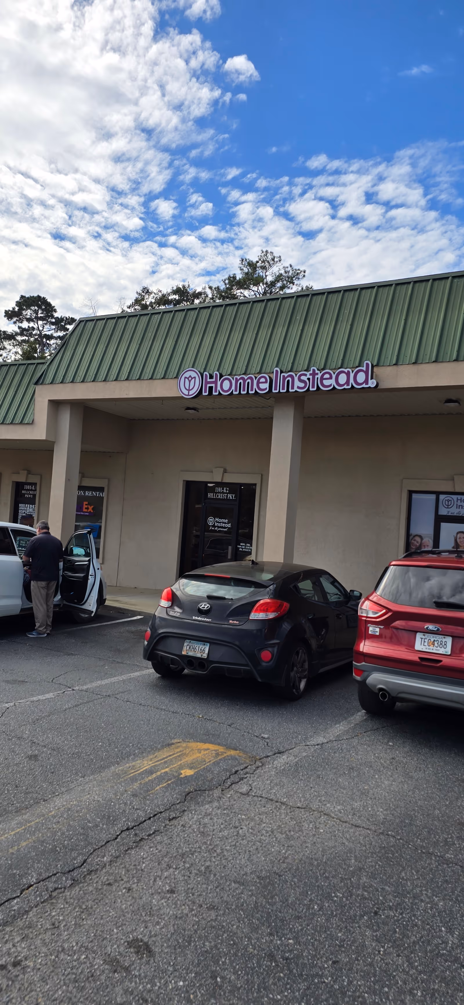 Front of a Home Instead facility with parked cars and a green awning.