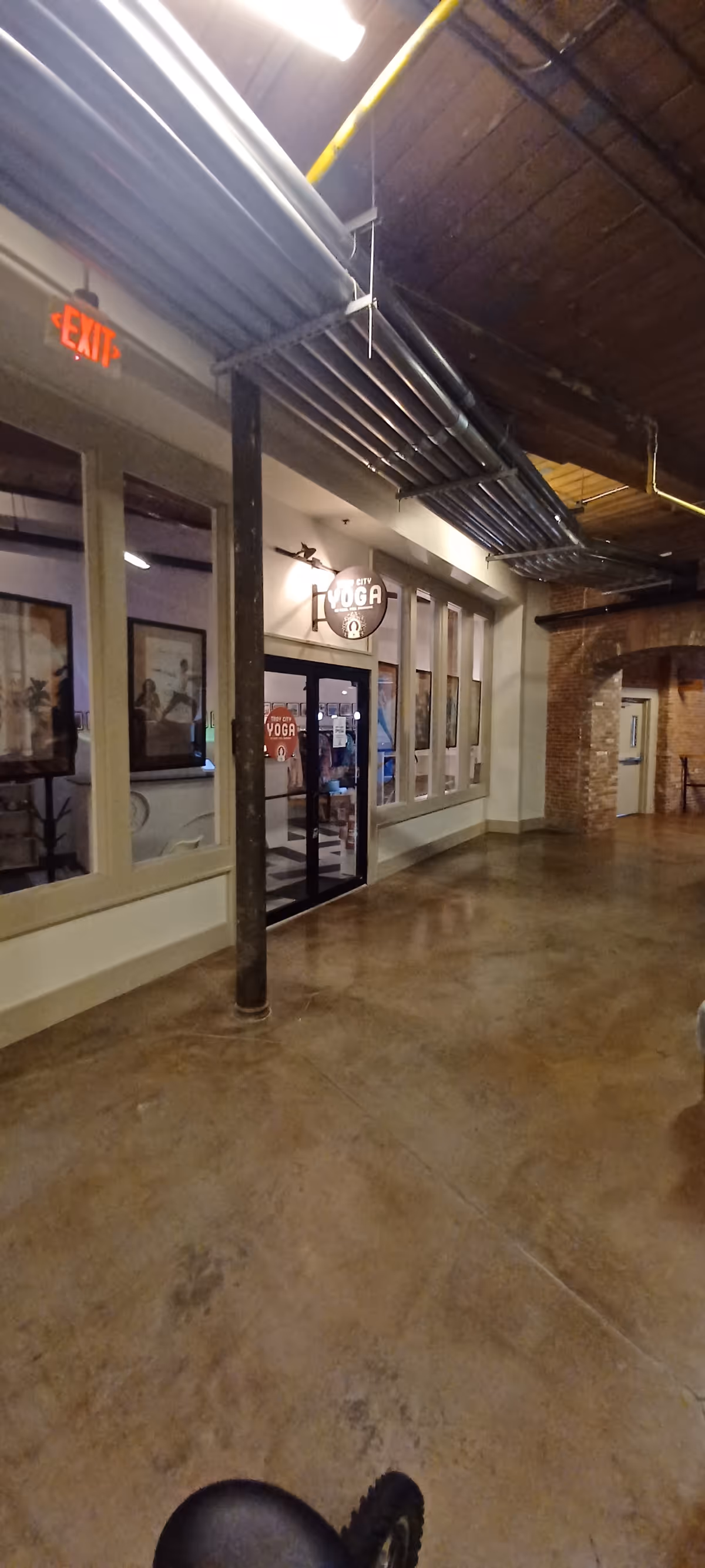Indoor corridor with exposed pipes, brick archway, and a yoga studio entrance.
