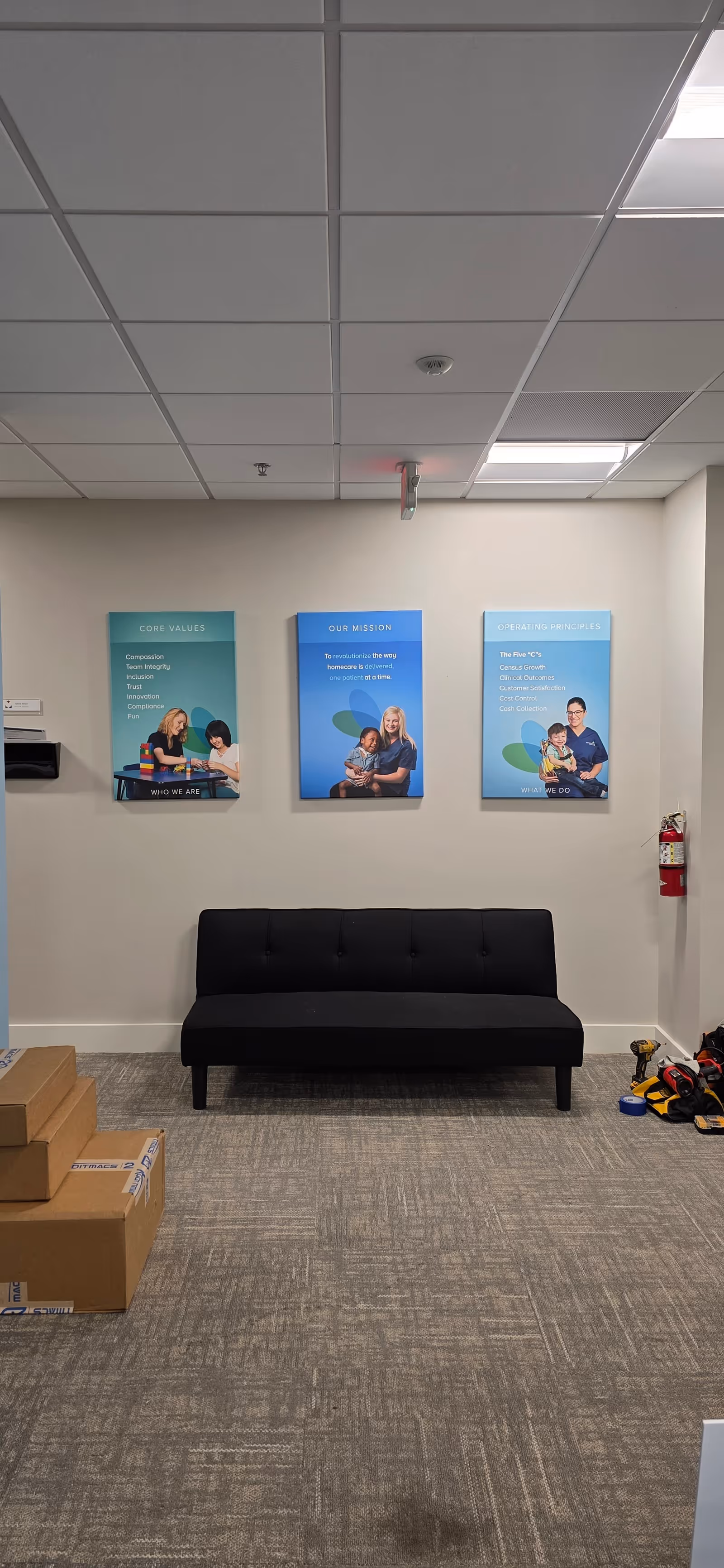 Interior reception area with a black sofa, wall posters, and stacked boxes.