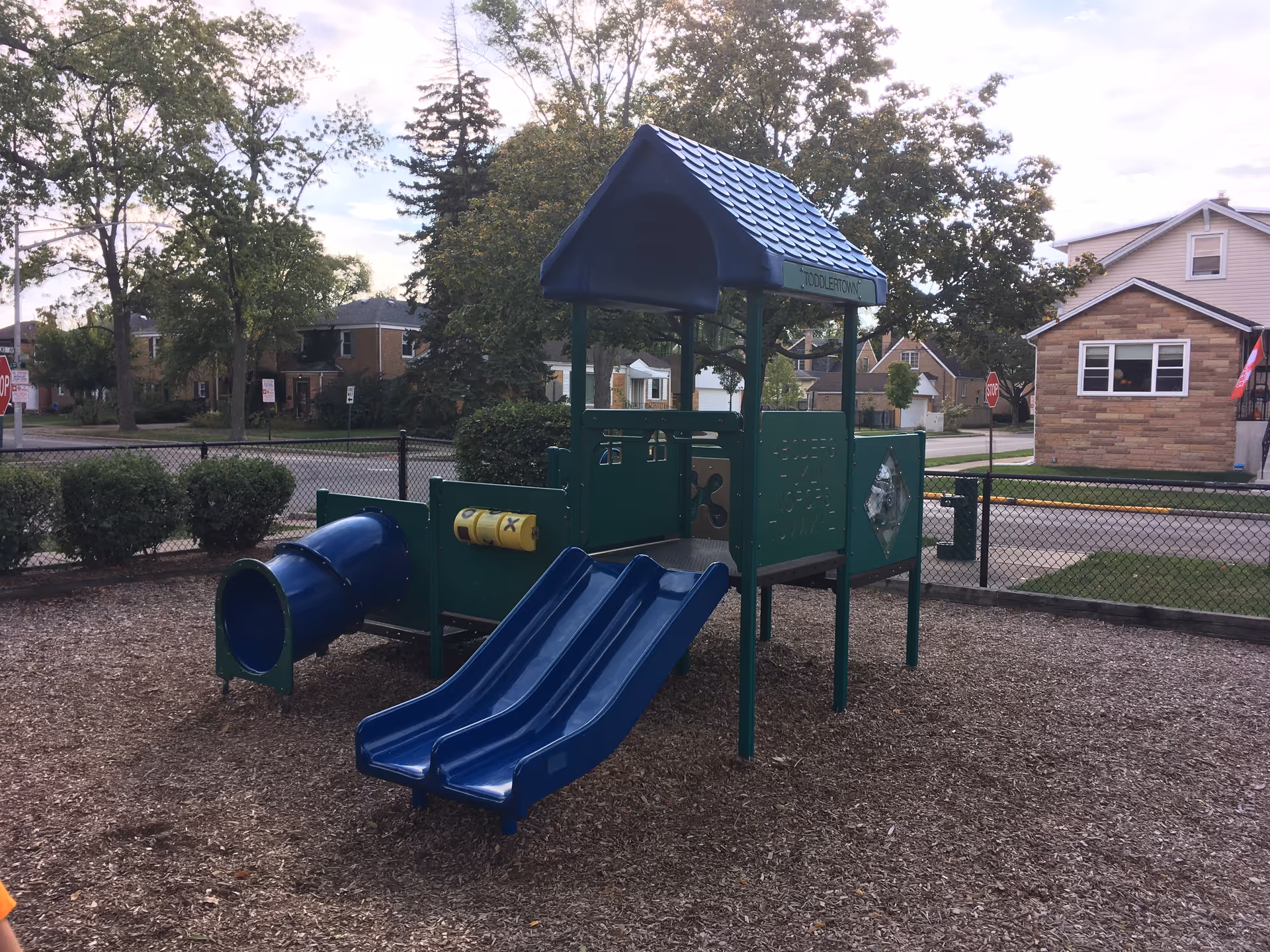 Colorful blue playground slides and a play structure in a fenced outdoor area.