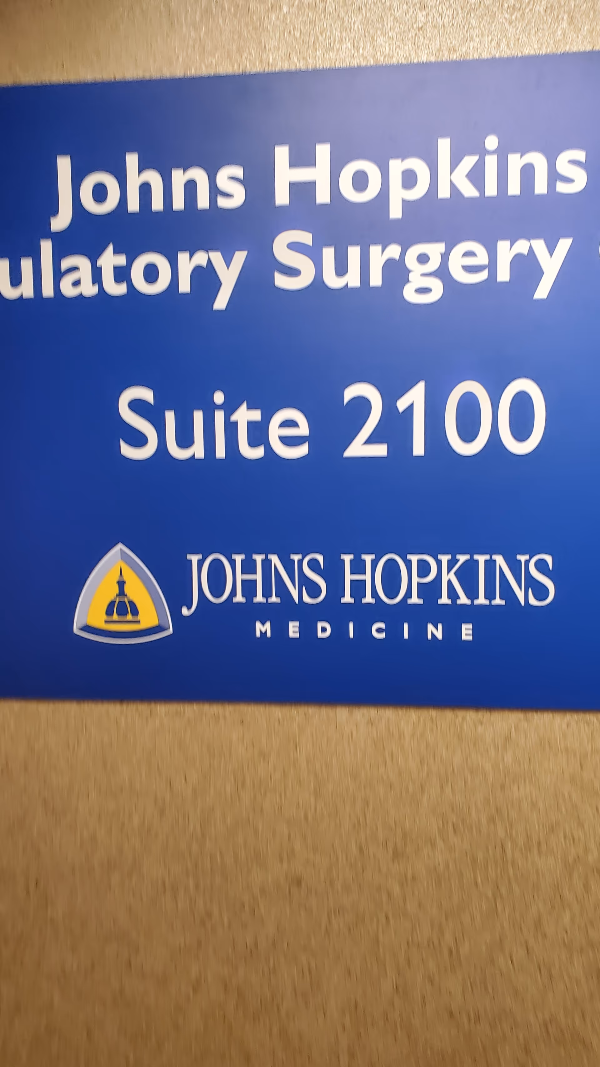 Blue Johns Hopkins Medicine sign reading Suite 2100 mounted on a beige wall
