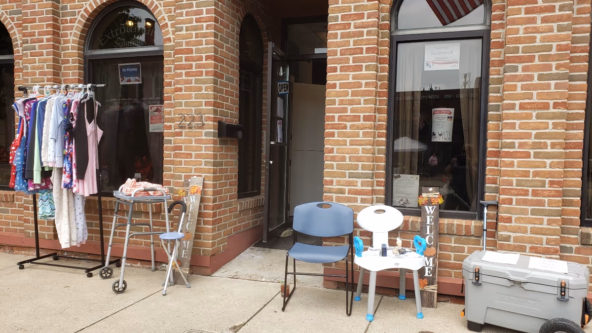 Exterior brick building with clothing rack, chairs, and welcome signs outside