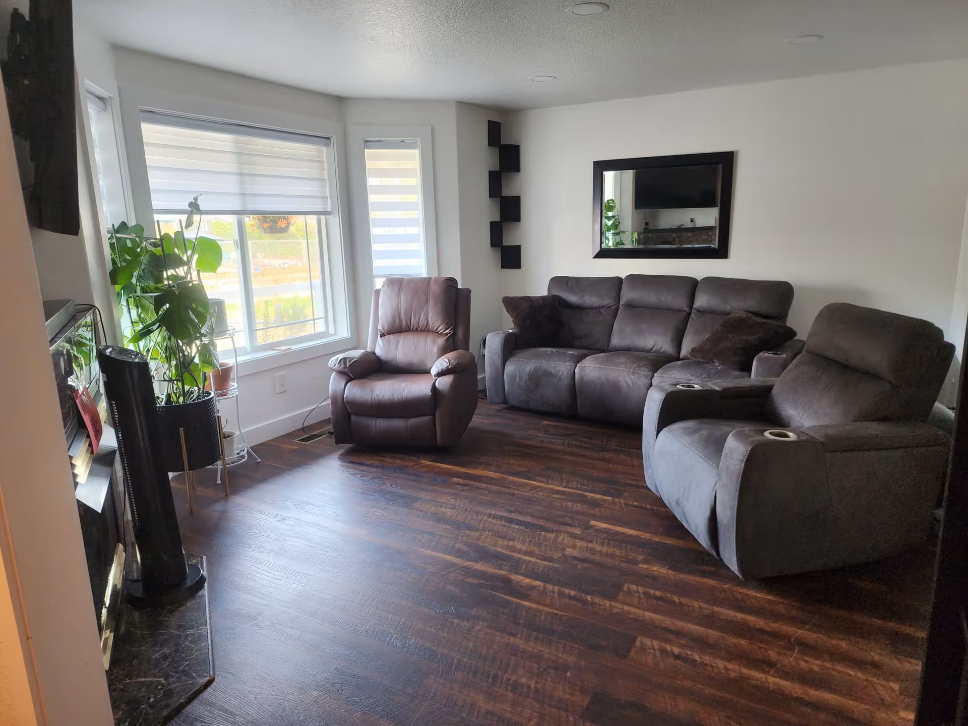 Cozy living room featuring dark leather seating, plants, and large windows.