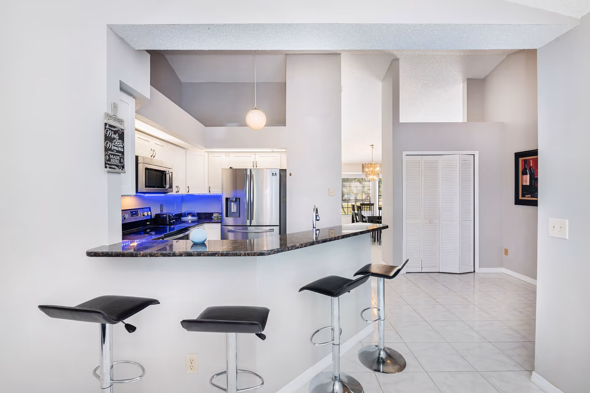 Modern kitchen with curved granite bar, three black stools, white cabinets, stainless appliances.