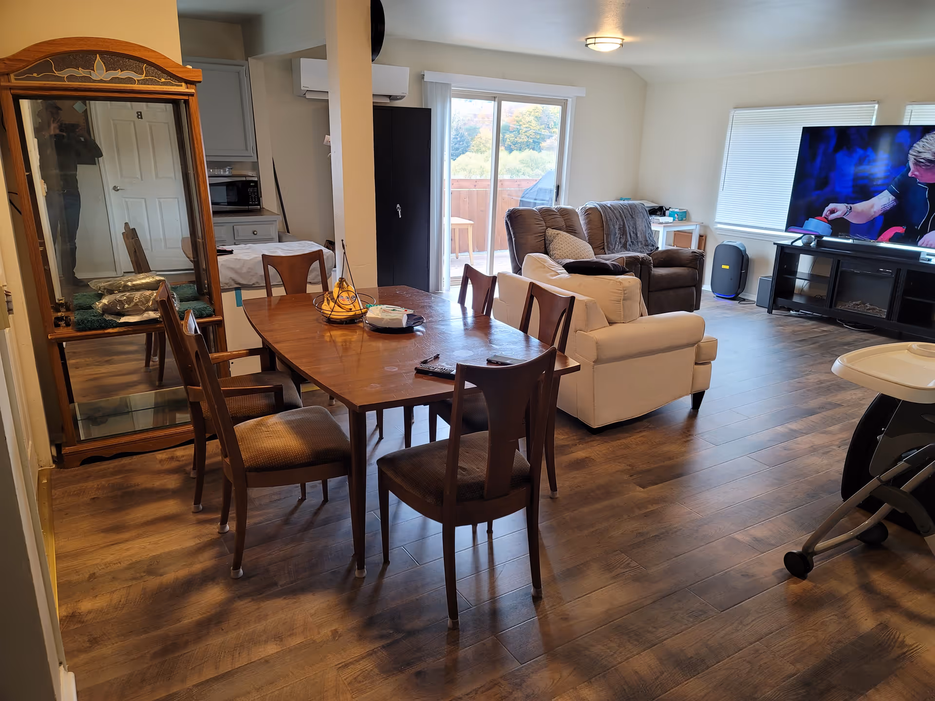 Open living and dining area with wooden table, chairs, sofa, TV, and sliding door.