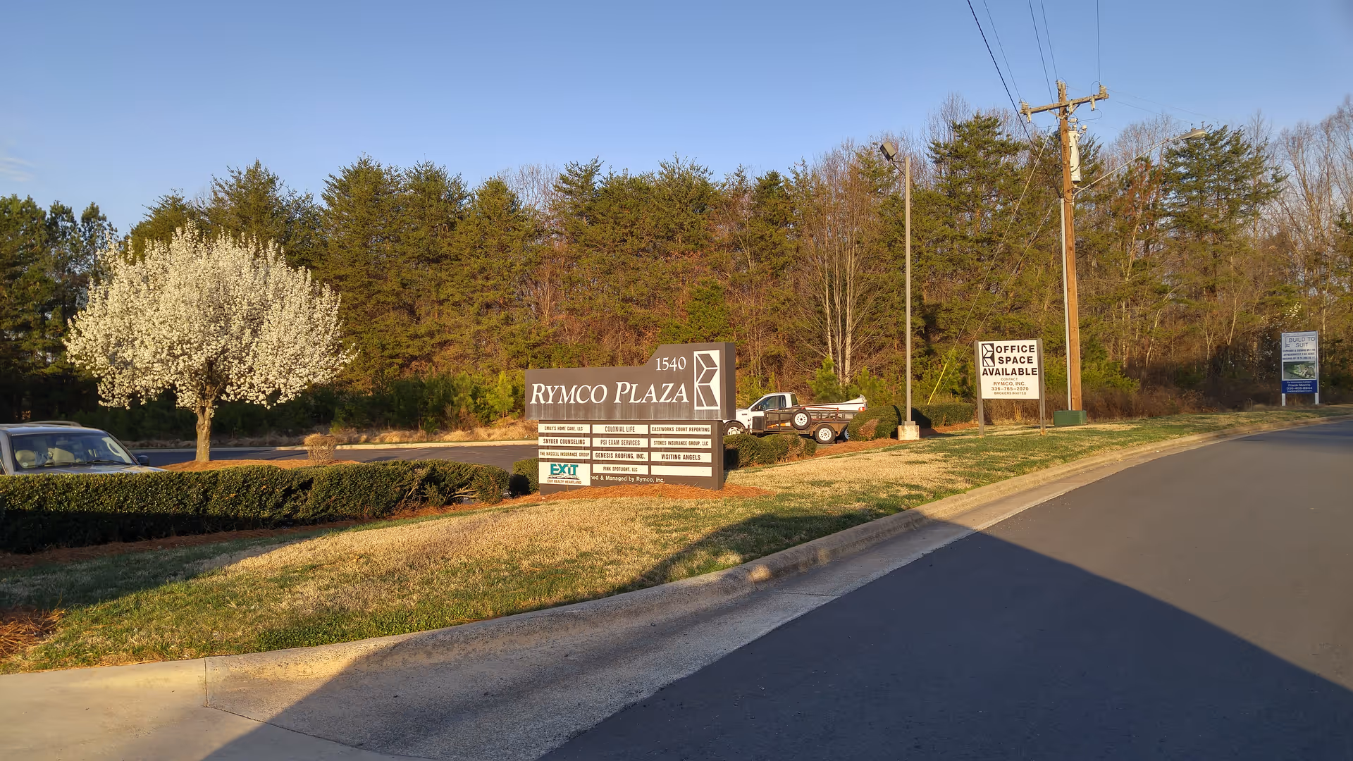 Exterior view of a road with a large RYMCO PLAZA sign and surrounding trees.