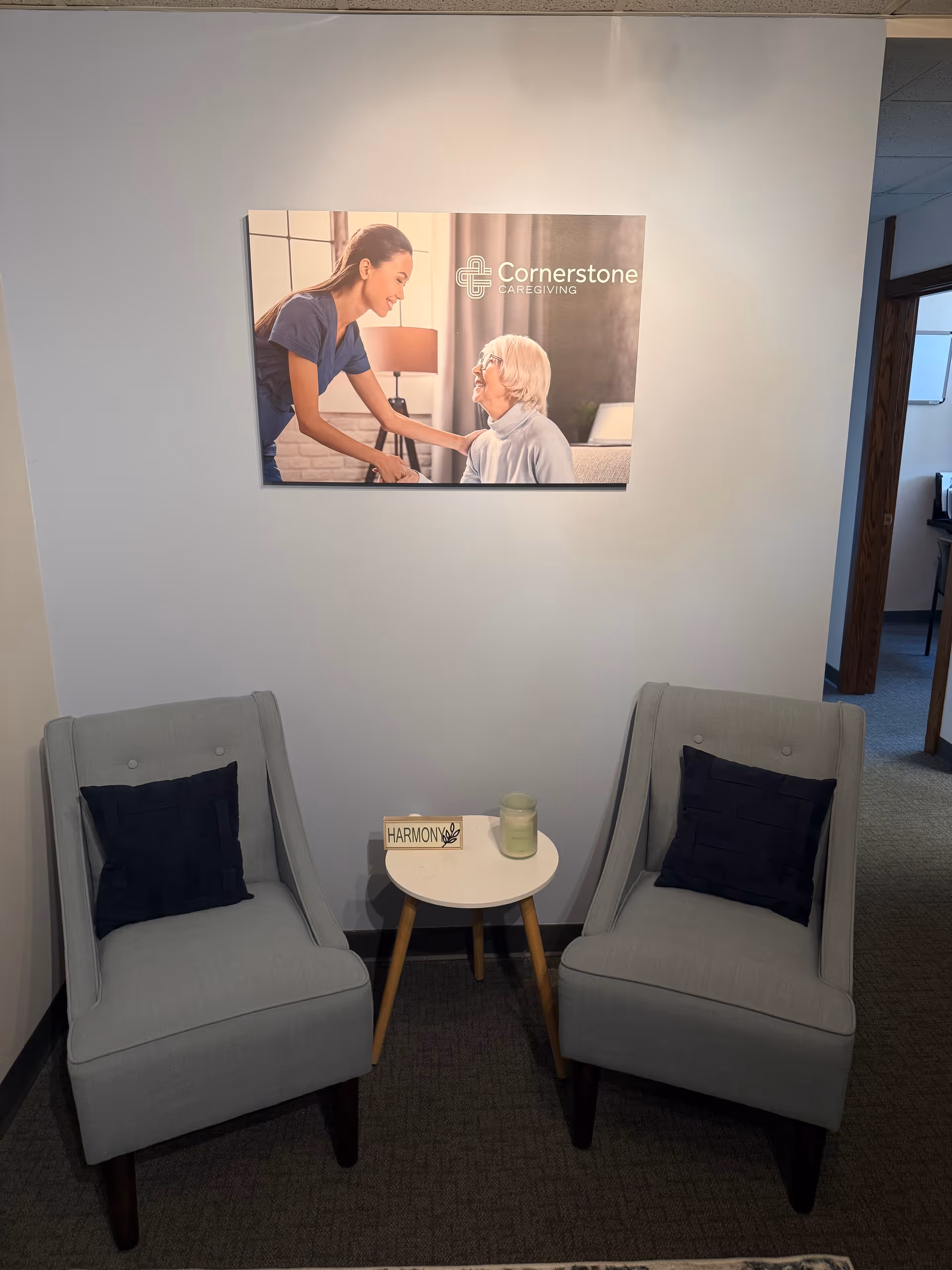 Waiting area with two light gray chairs, a round table, and wall art featuring Cornerstone Caregiving.