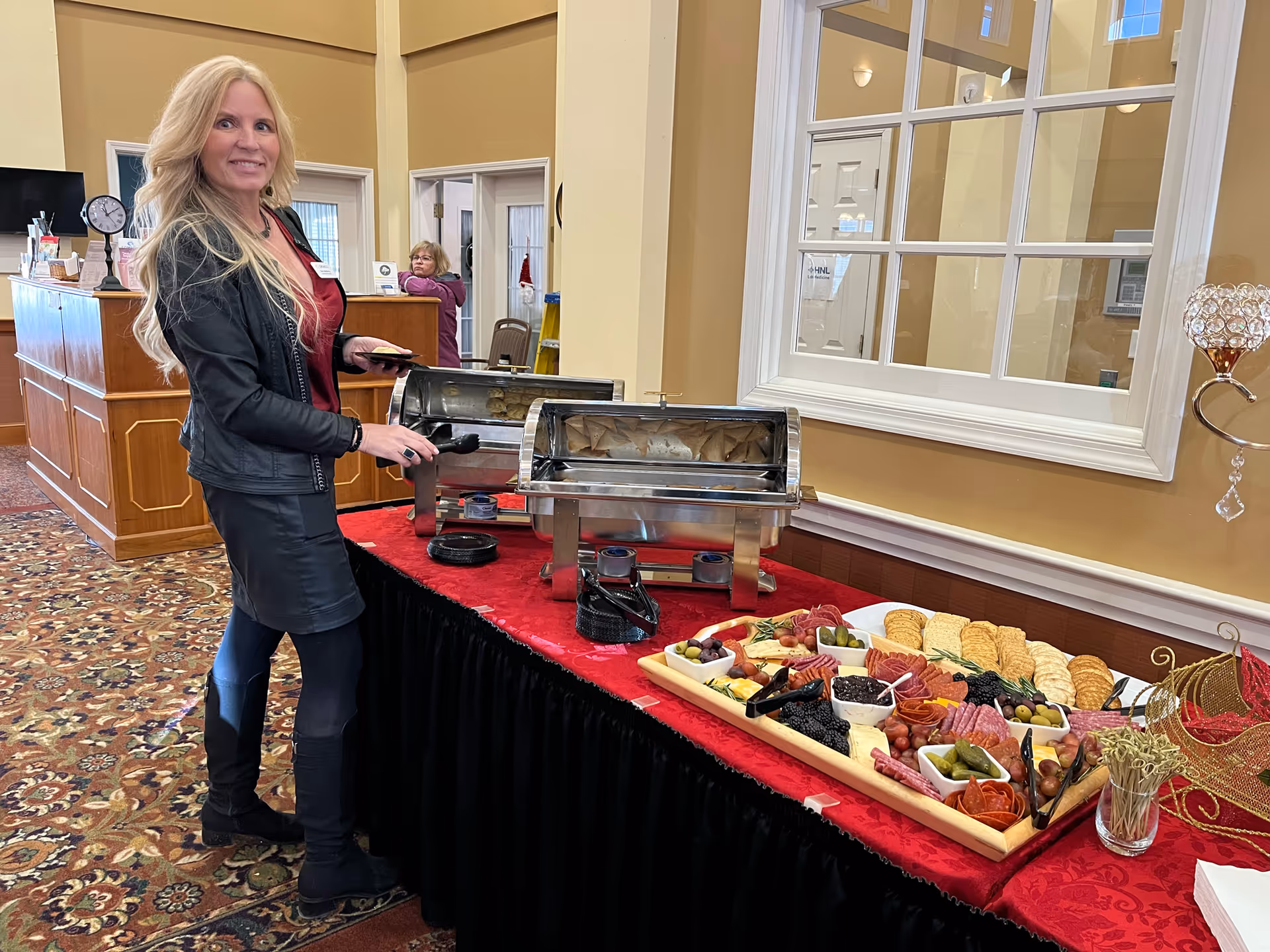 Staff member serves buffet in a senior facility dining area with a side table of appetizers.