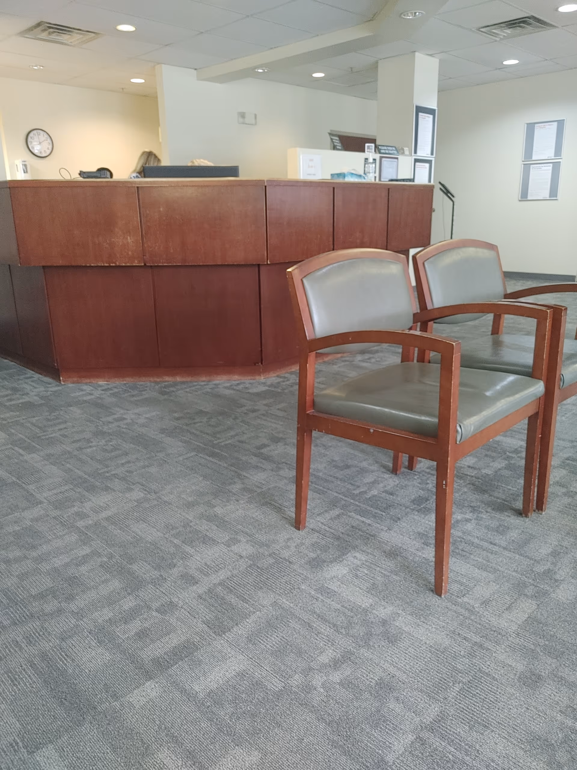 Indoor reception area with a curved wooden counter and two upholstered chairs.