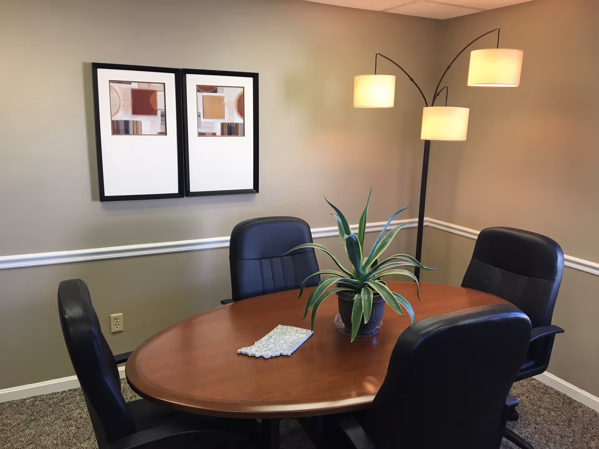 Round wooden table with four black chairs, plant centerpiece, and arched floor lamp in a room.