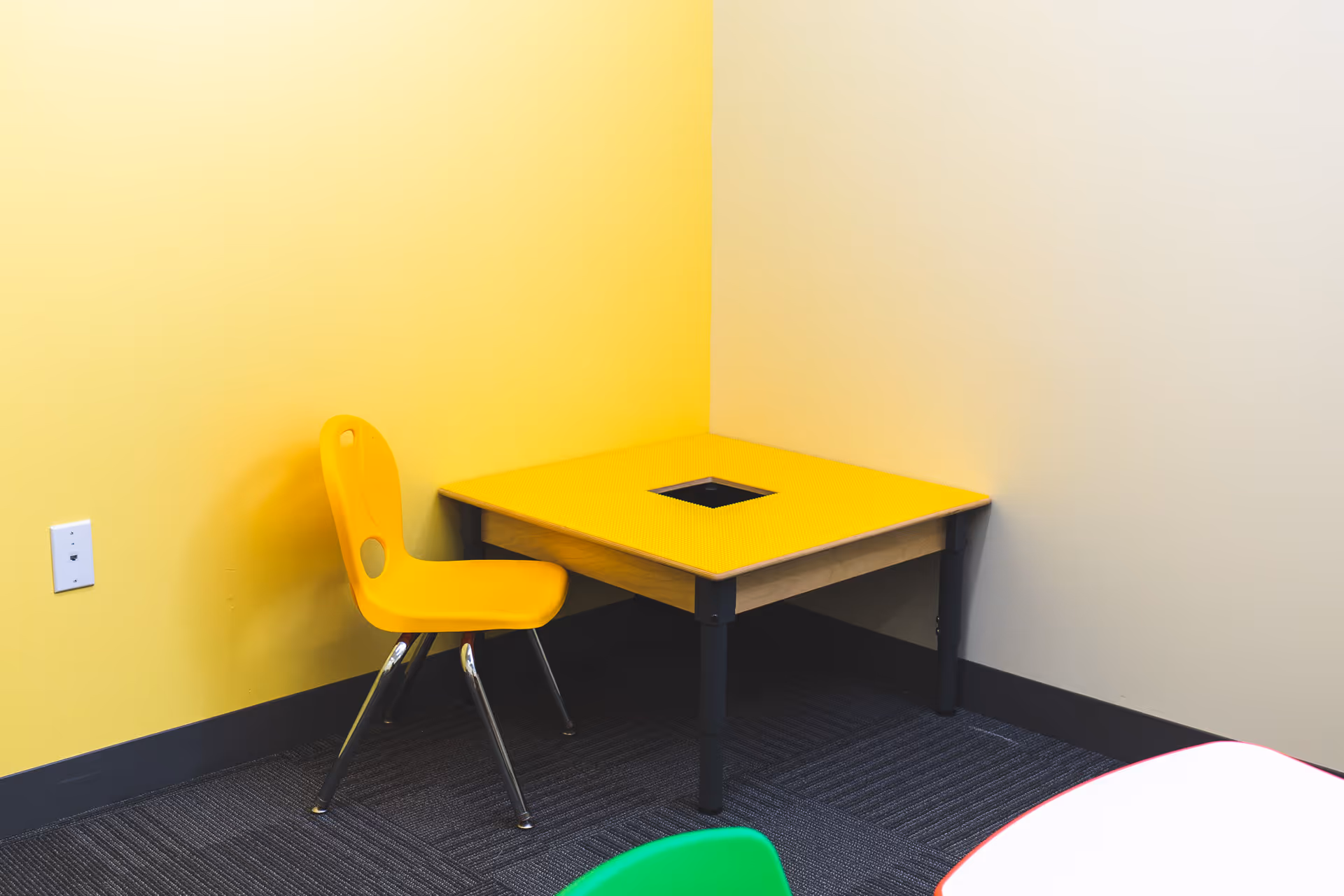 A yellow chair beside a yellow table with a central hole in a yellow-walled room.