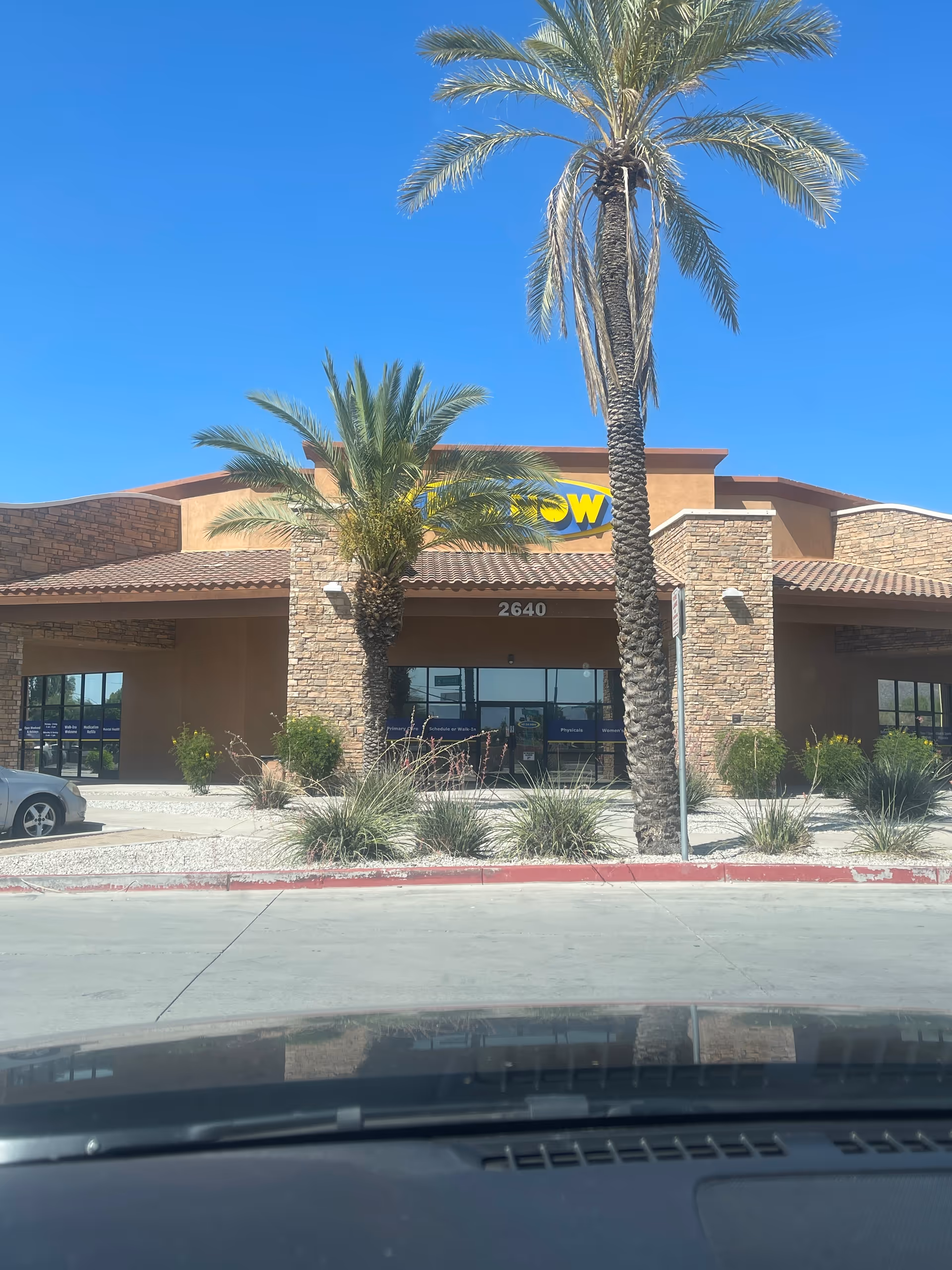 Exterior view of a MY DR NOW clinic with palm trees and clear blue sky.