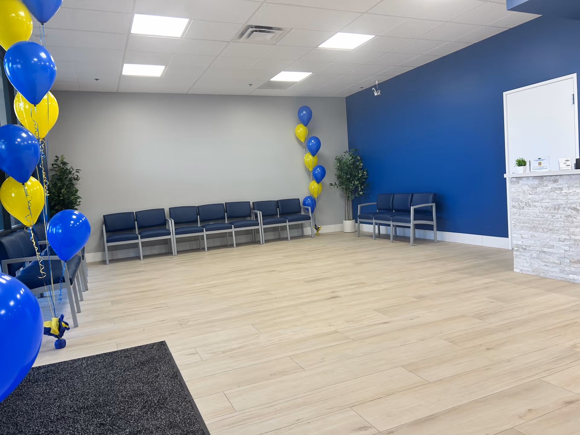 Bright senior living lobby with blue walls, rows of chairs, and blue-yellow balloons.