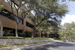 Exterior view of a brick building with steps, trees, and a parking area.