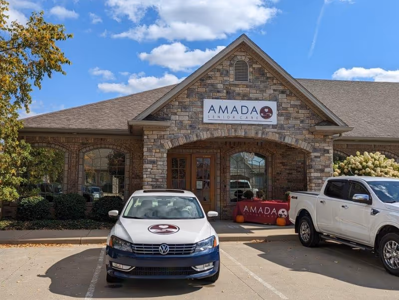 Stone-faced Amada Senior Care building exterior with two parked cars in front.