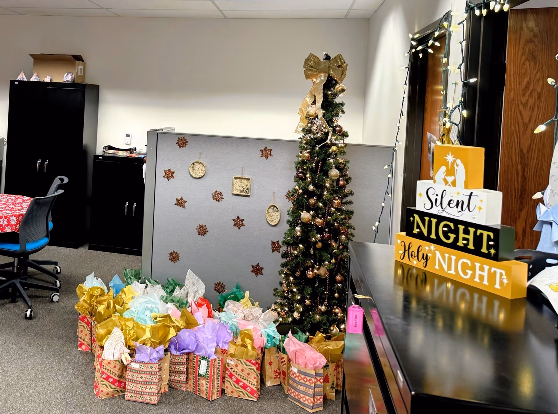 Office area with Christmas tree, gift bags, string lights, and festive signage.