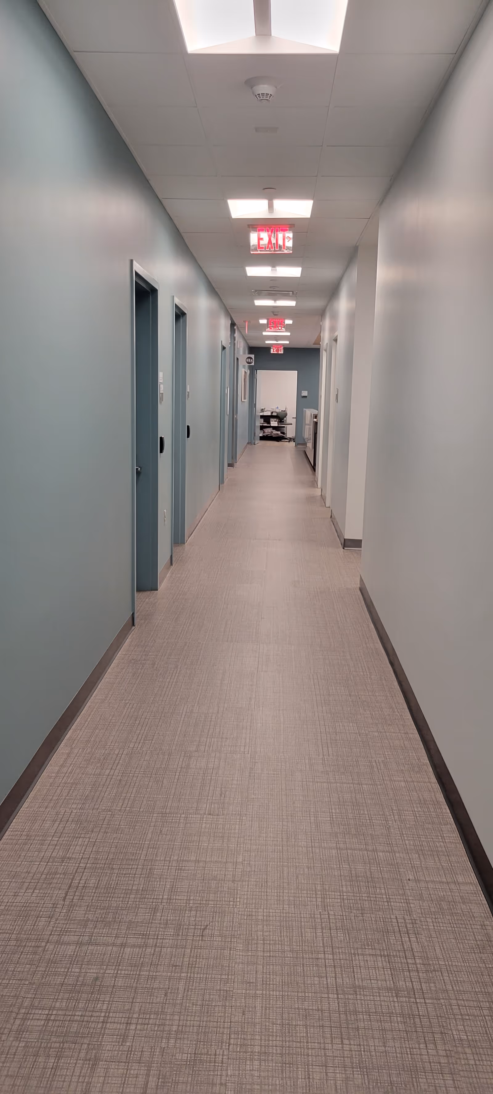 Long hallway in a facility with teal walls and exit signs.