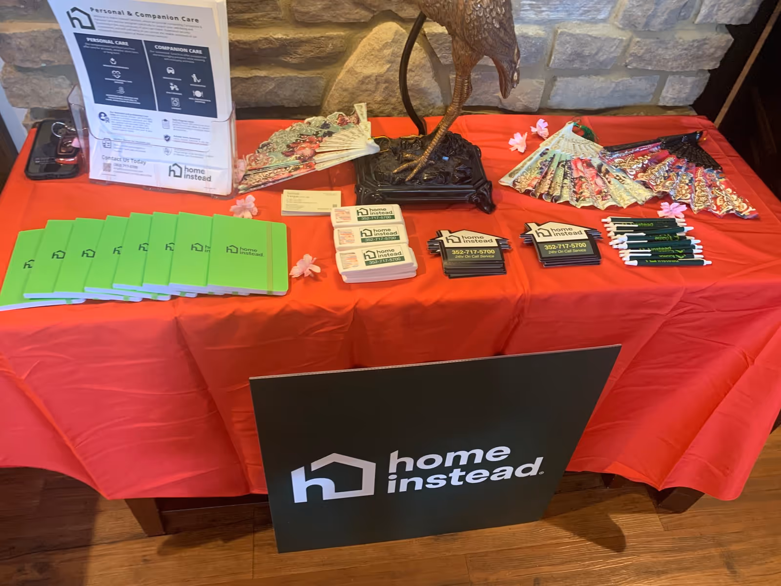 Promotional display table with Home Instead brochures, business cards, and pens on red cloth.