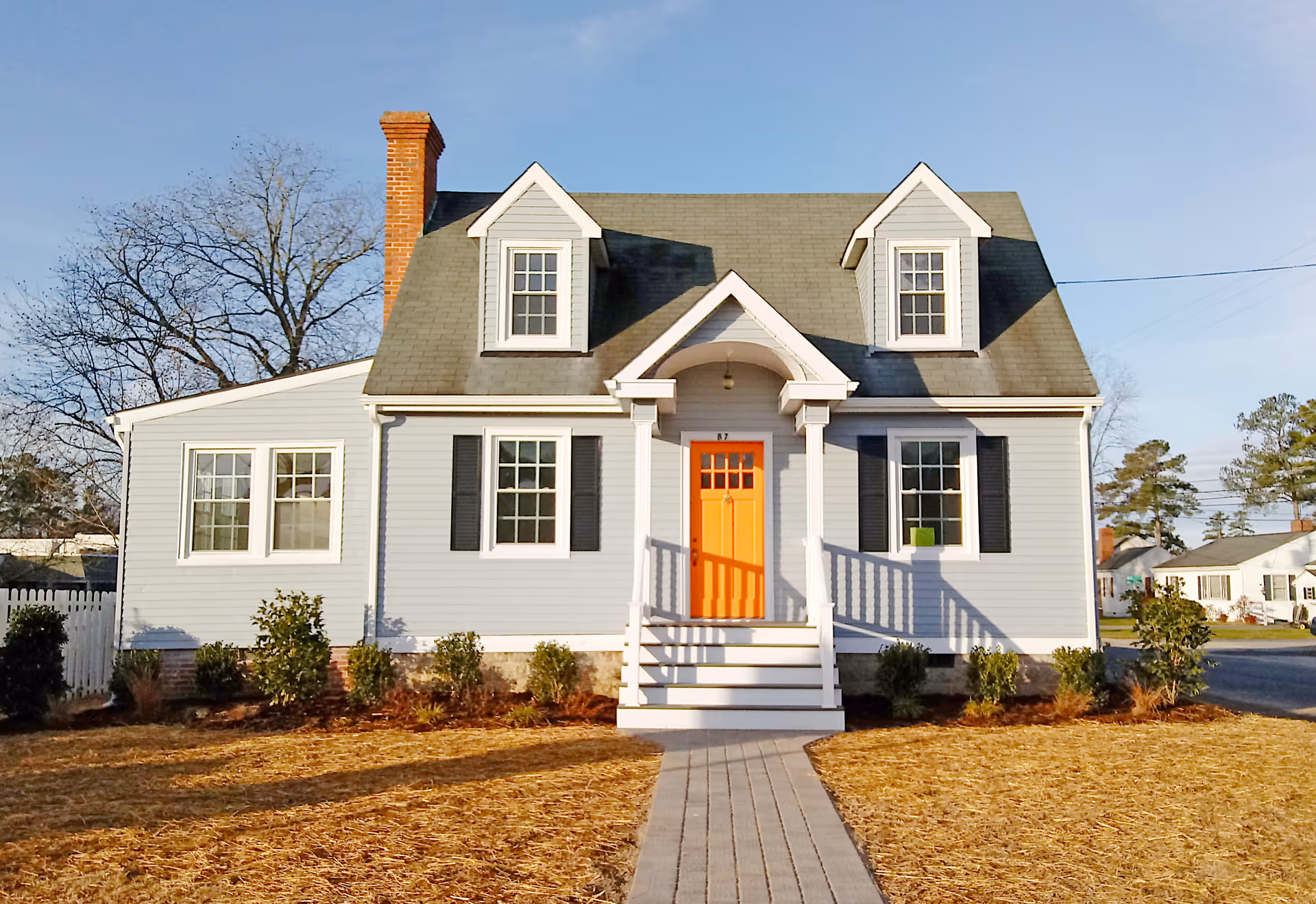 Front view of a light blue house with orange door, white porch, and steps.