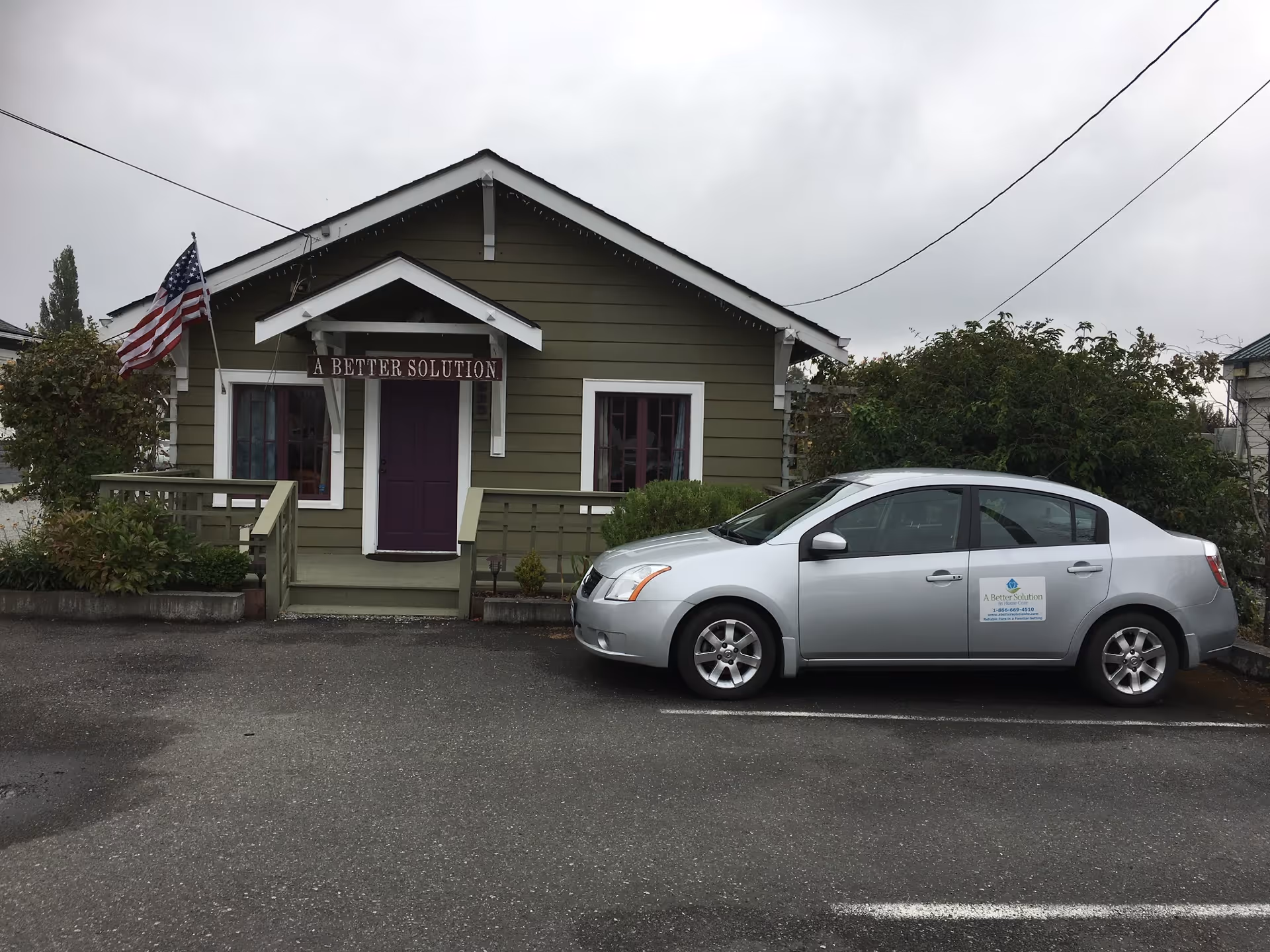 Exterior view of a green building with a purple front door and a parked silver car.