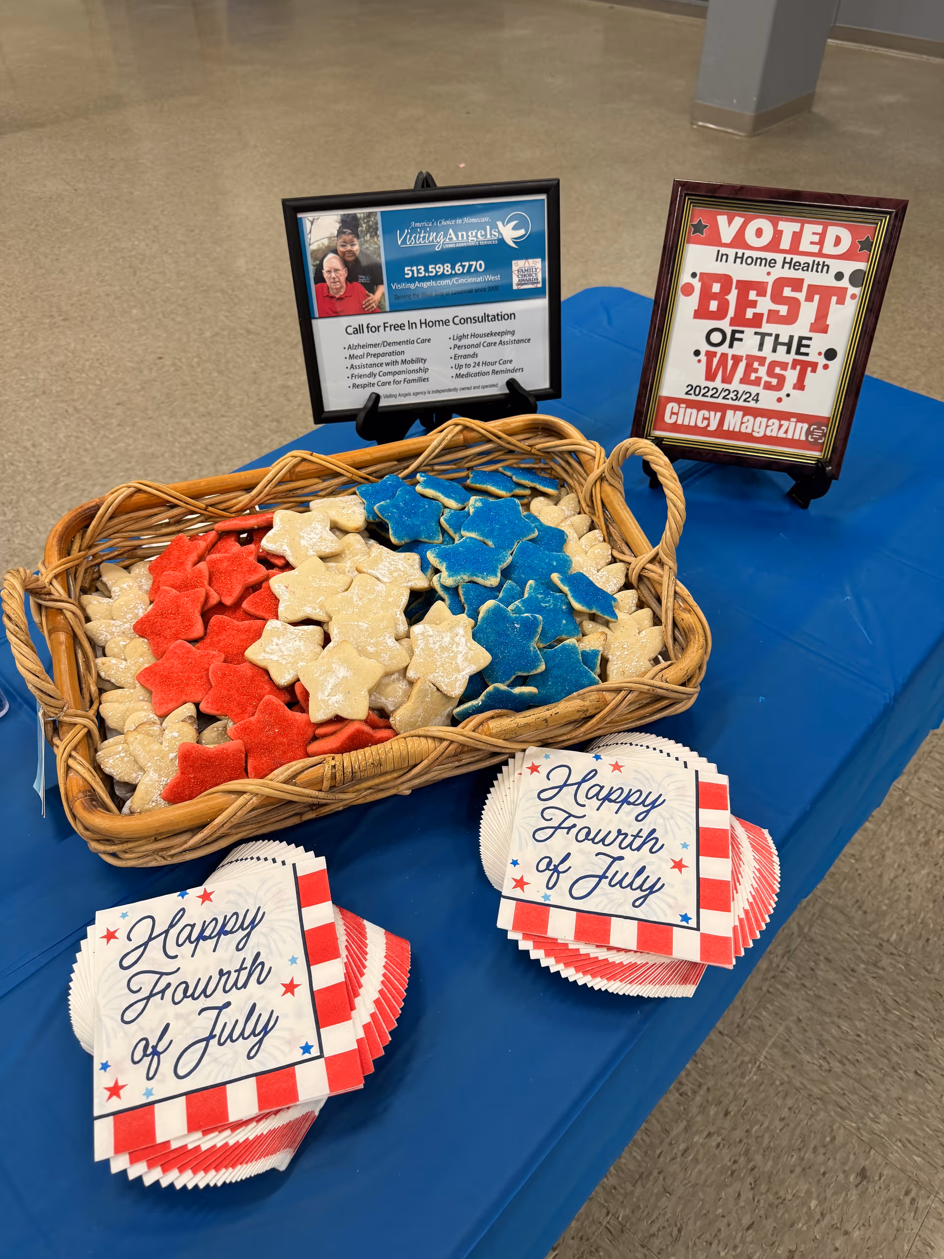 Table displays Fourth of July cookies and Visiting Angels promotional signs indoors.