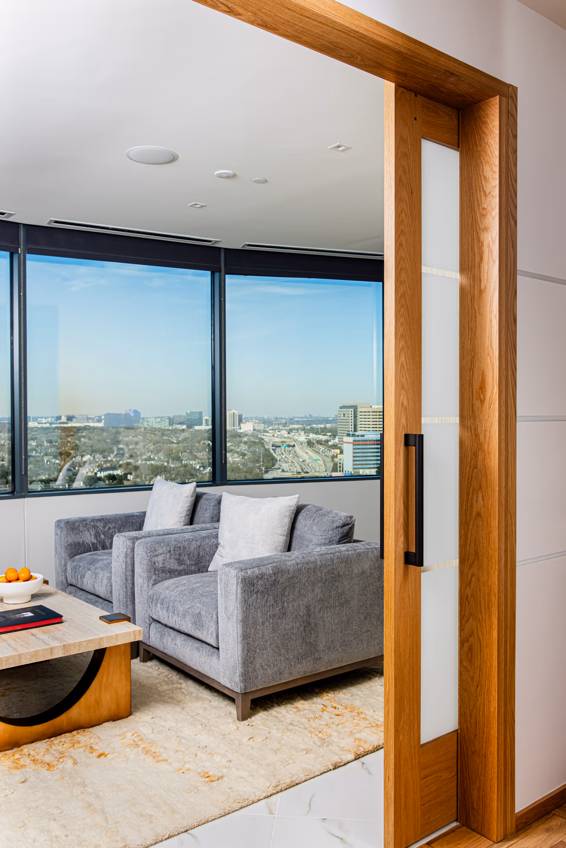 Modern lounge area with two gray armchairs beside a large window overlooking the city.