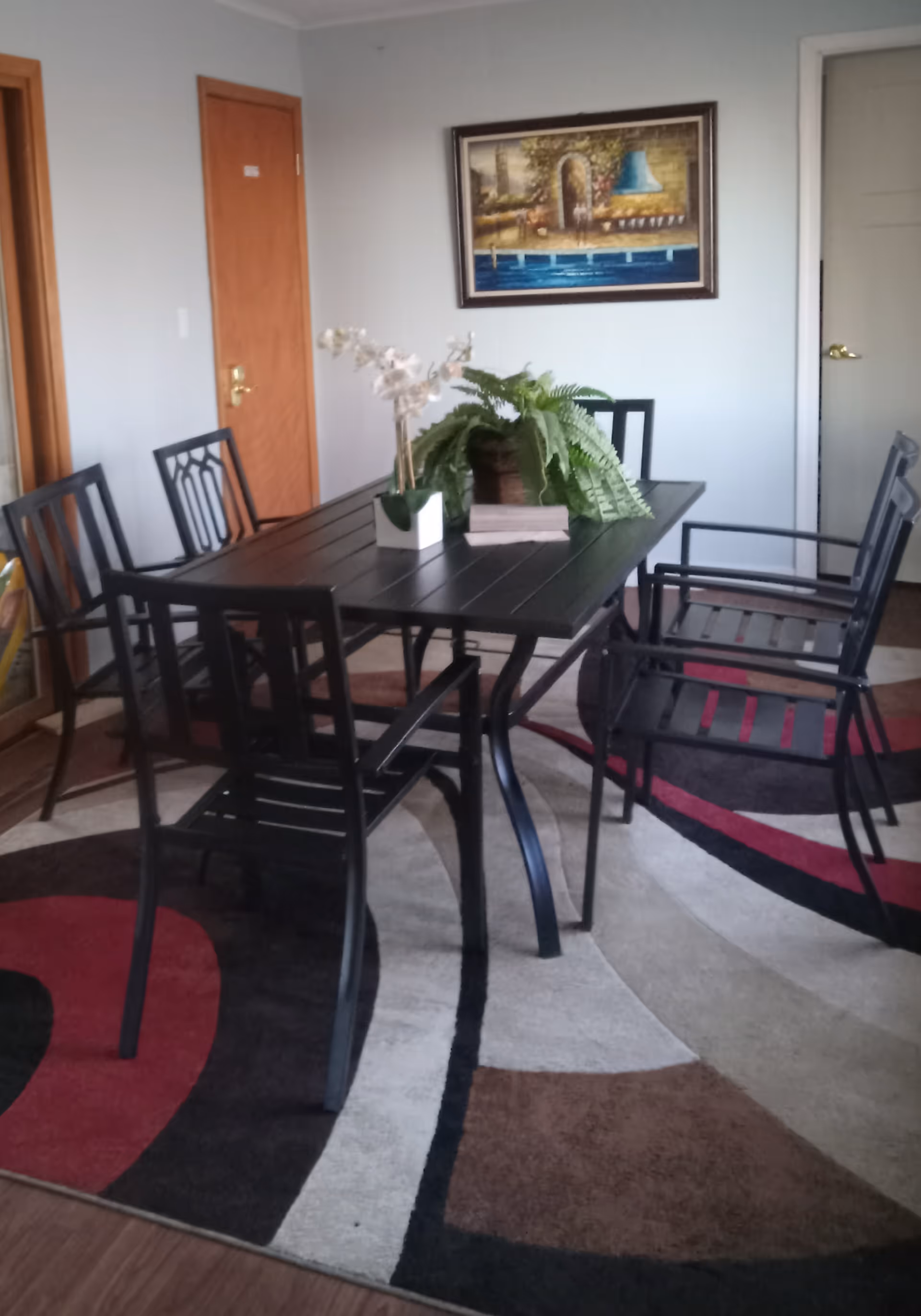 Black dining table with six chairs, potted plants, and wall art in a cozy dining room.