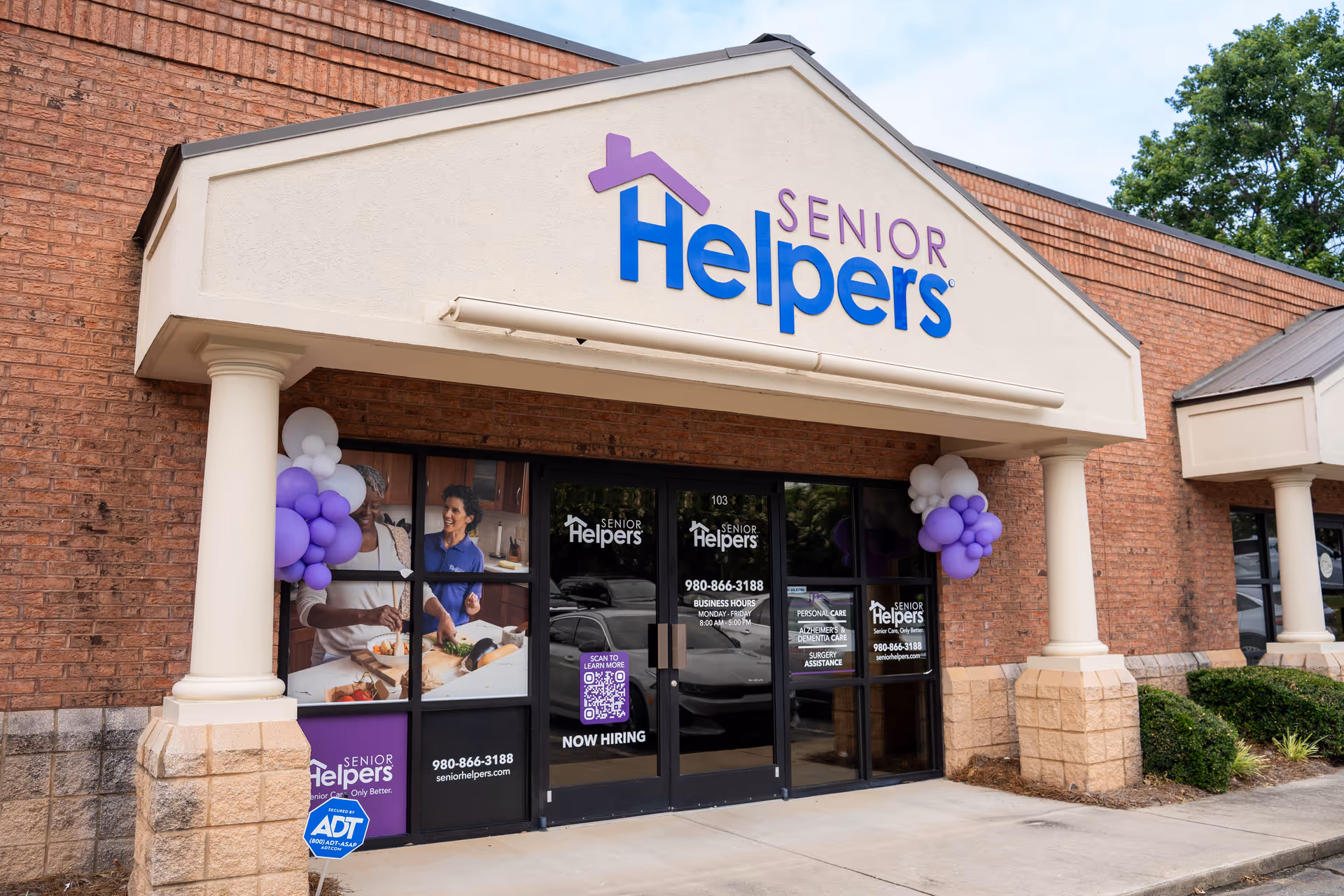 Exterior of a Senior Helpers facility with a sign, balloons, and glass entrance doors.
