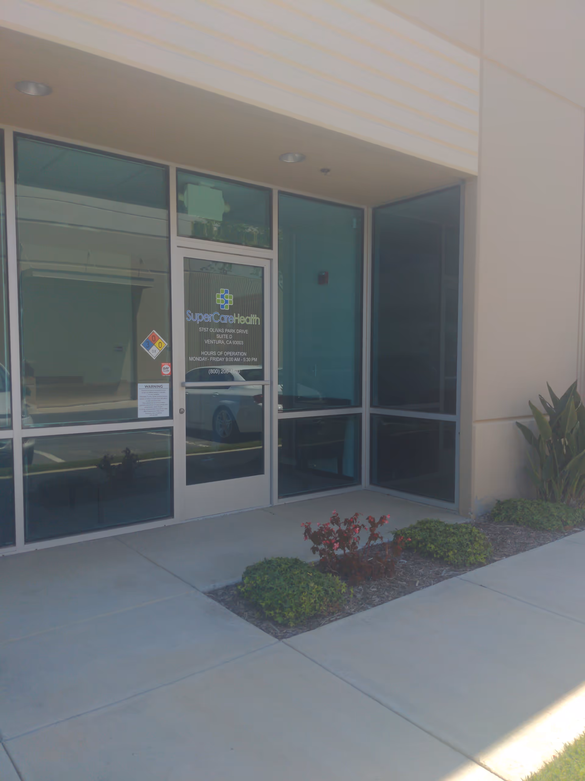 Front entrance of SuperCare Health clinic with glass doors and surrounding landscaping.