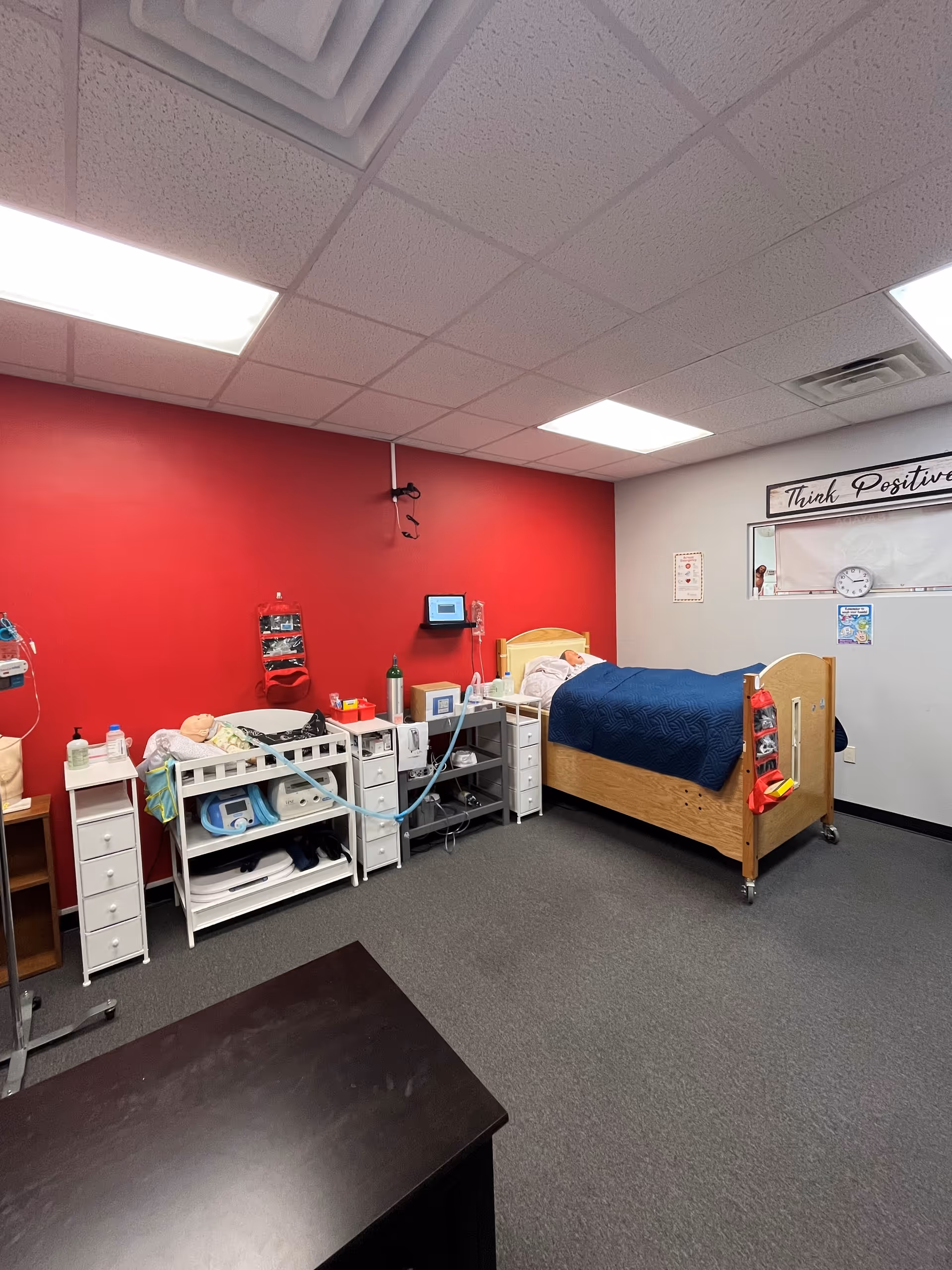 A medical care station and patient bed inside a clinical room with a red wall.