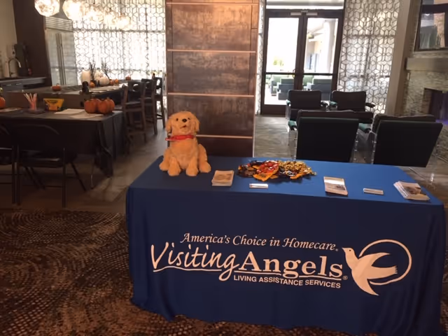 Blue Visiting Angels display table in a modern lobby with a plush dog.