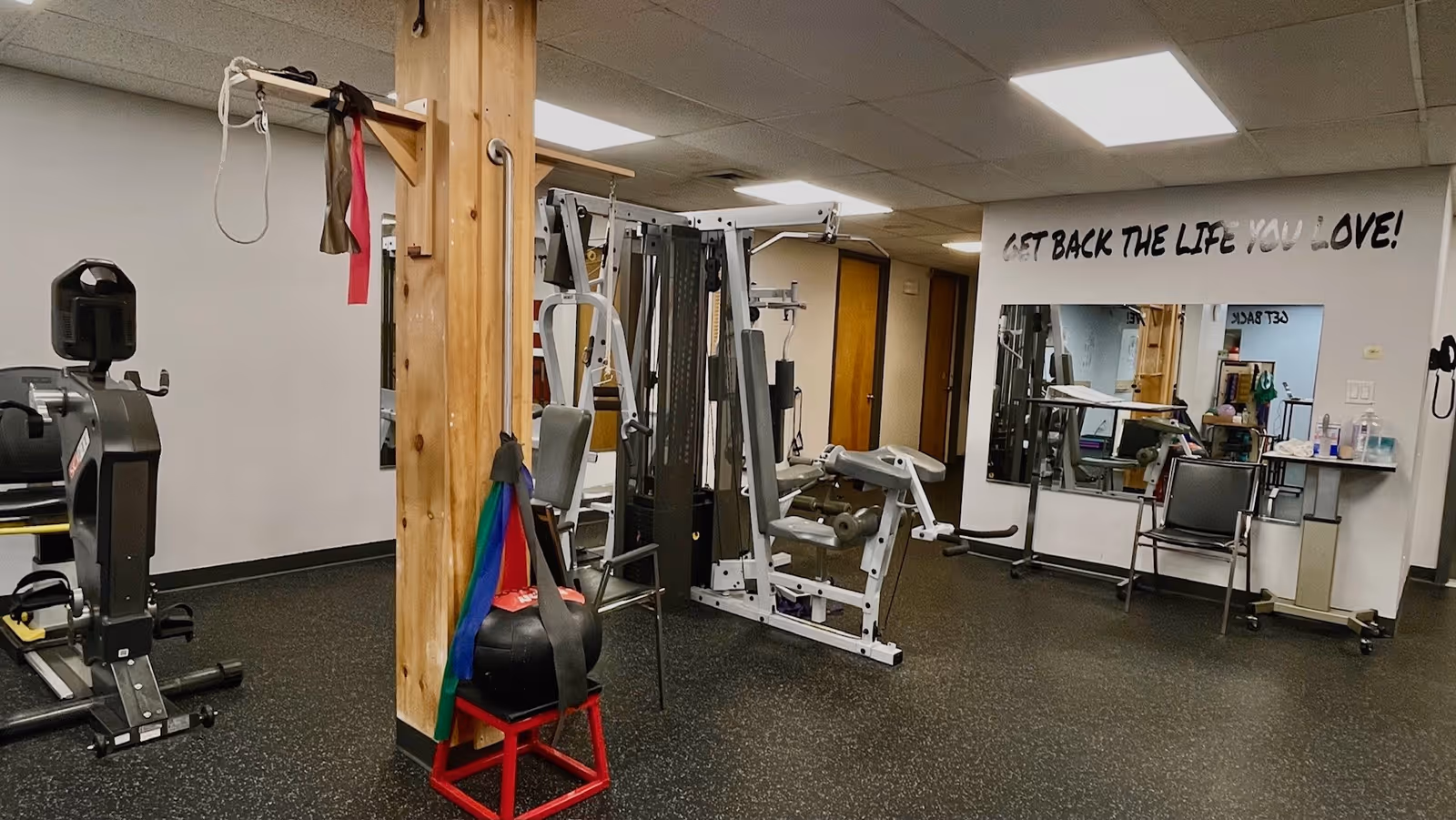 Indoor gym area in a senior living facility with equipment and mirrors.