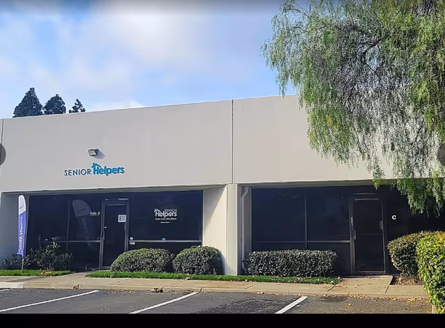 Exterior view of a Senior Helpers storefront with glass windows and shrubs.