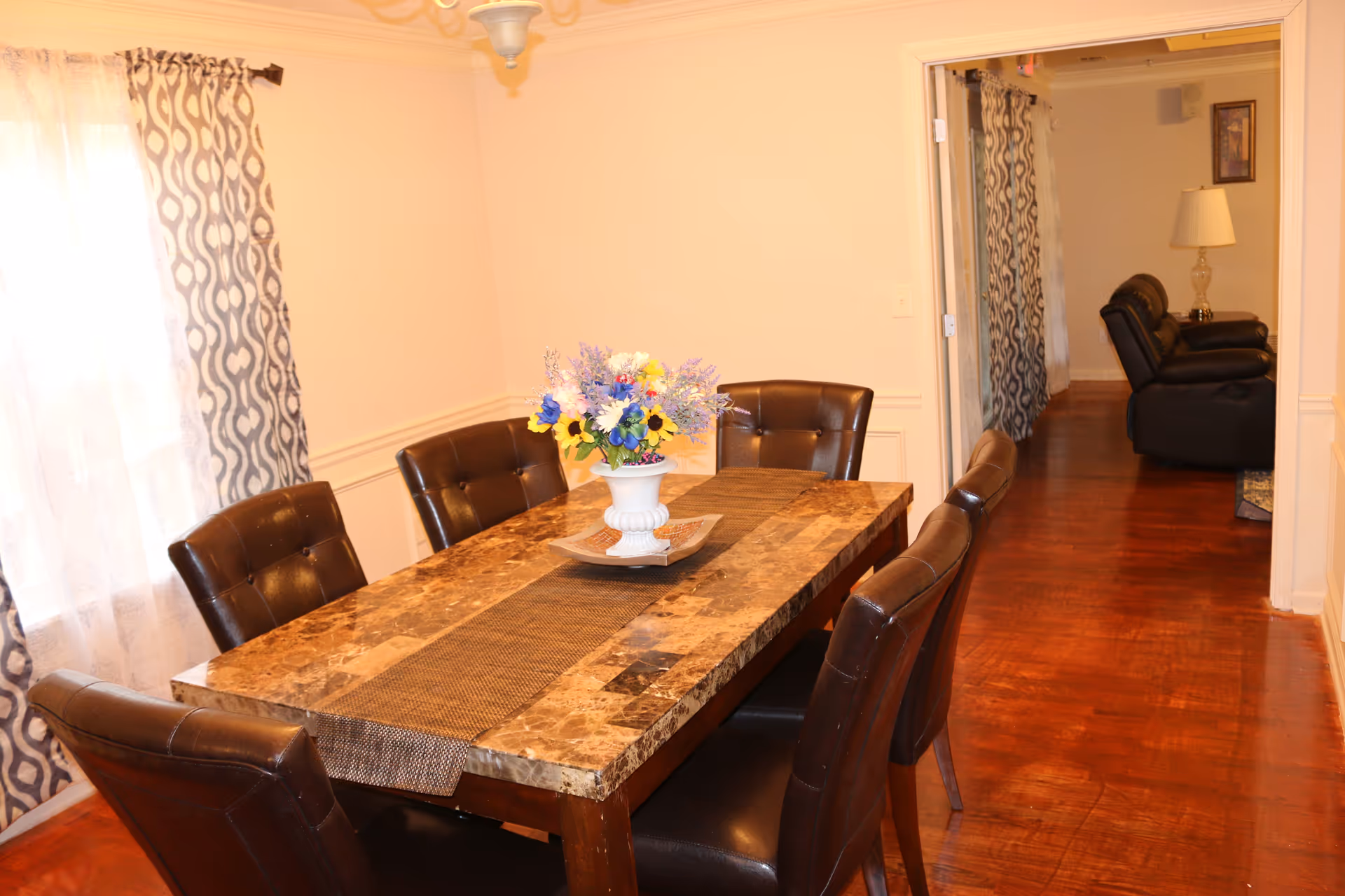 Bright dining room with a marble table, brown chairs, and a hallway to the living area.